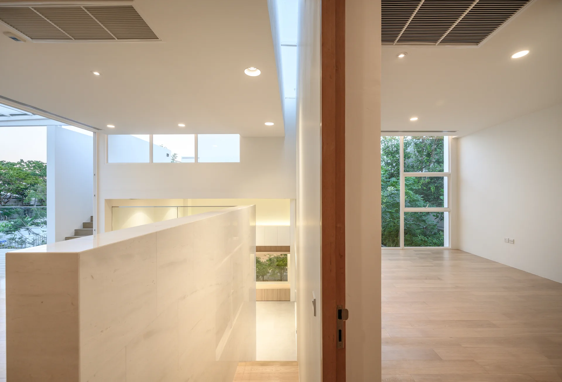 A minimalist residential landing with light wood flooring, a central marble partition wall, and a linear ceiling skylight.
