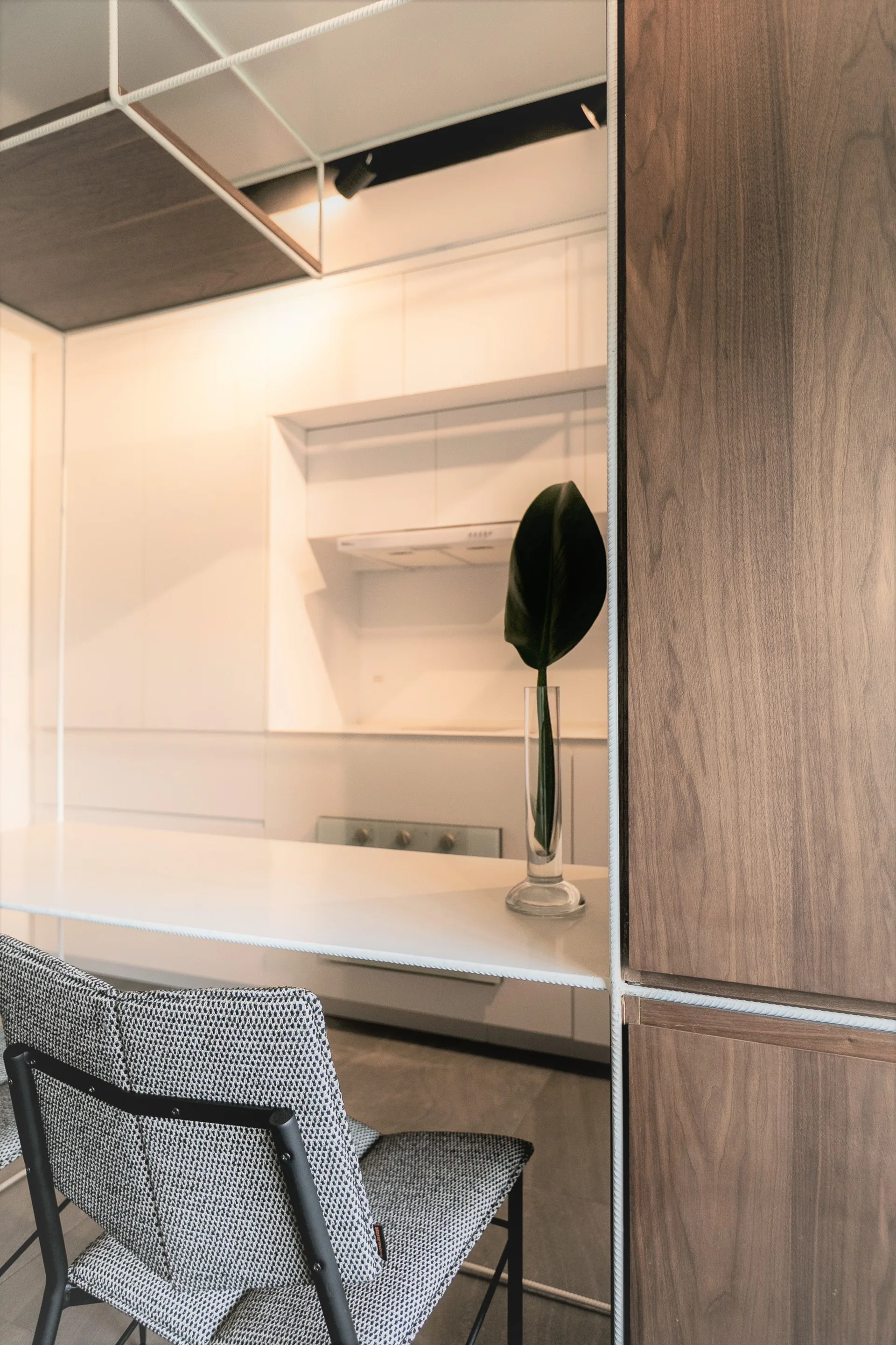 A modern kitchen featuring sleek white cabinetry, a large wood-paneled accent wall, a white countertop, and a textured grey dining chair.