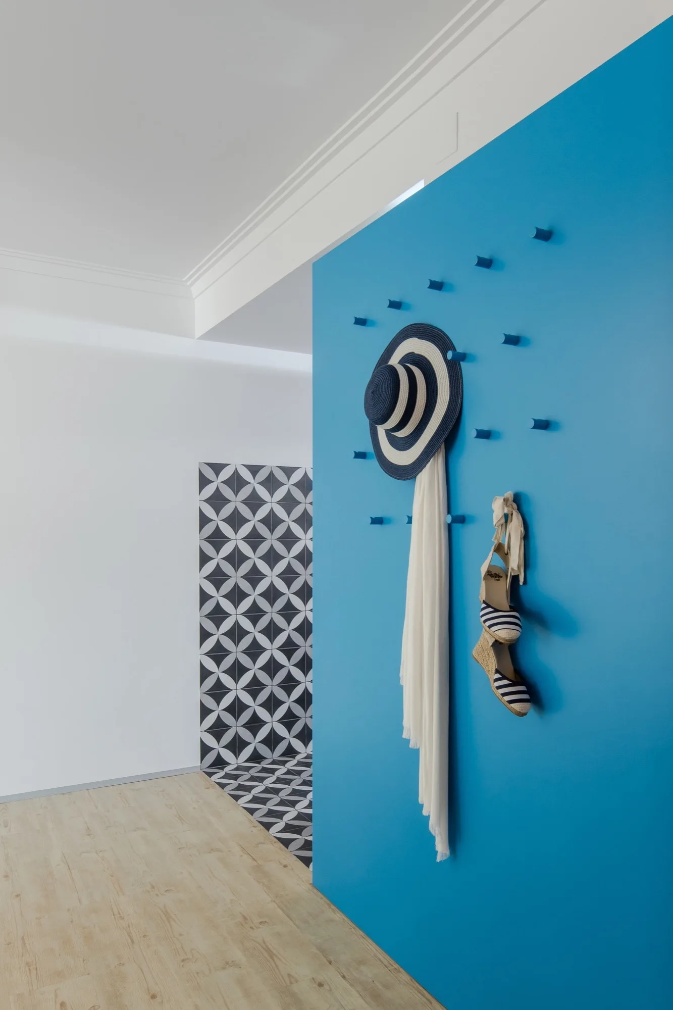 A bright blue accent wall in an entryway features integrated wall pegs displaying a striped sun hat, white scarf, and striped shoes.