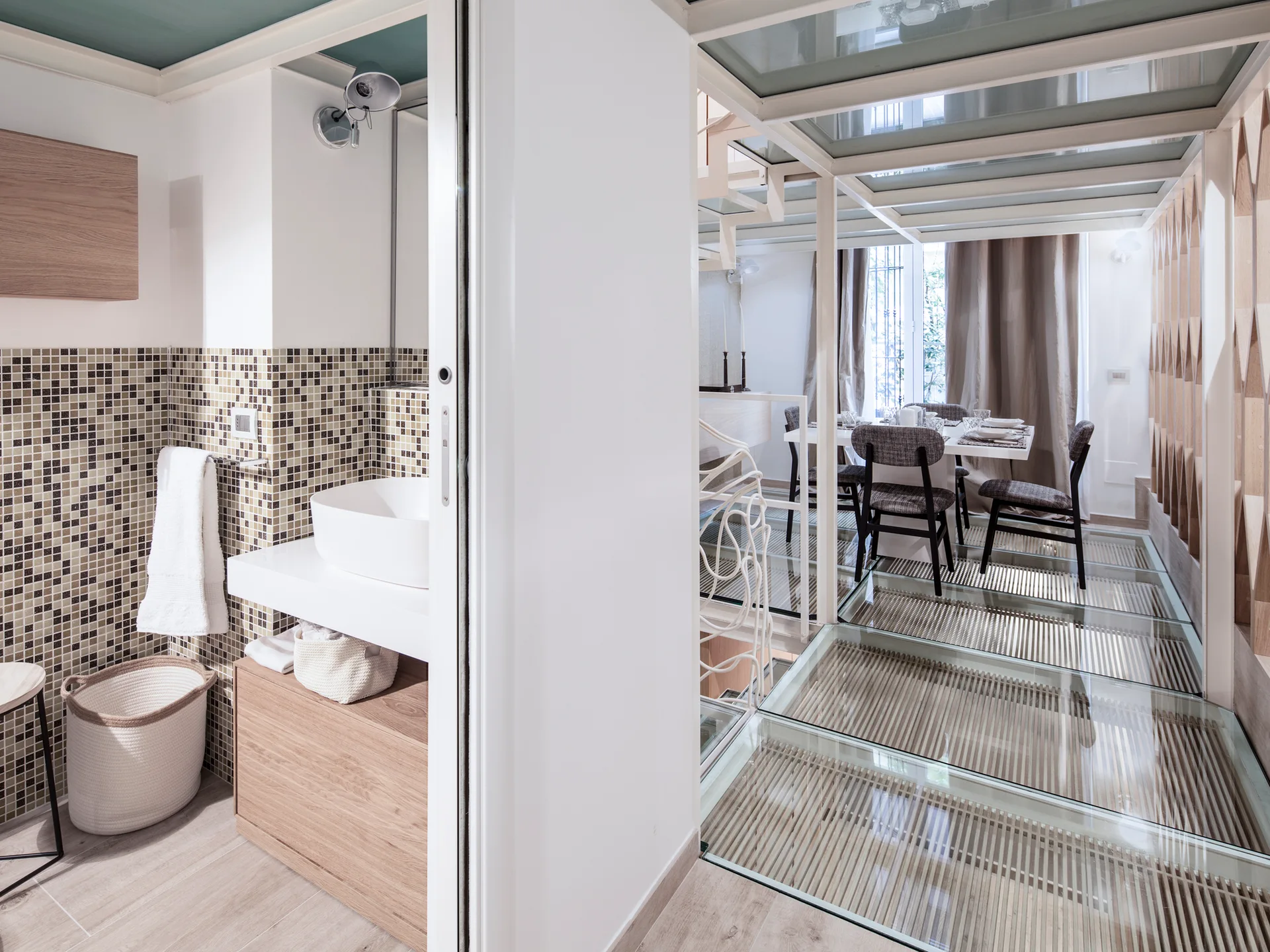 A modern bathroom features a vessel sink and mosaic tile wall next to a dining area with structural glass floor panels over wood slats.