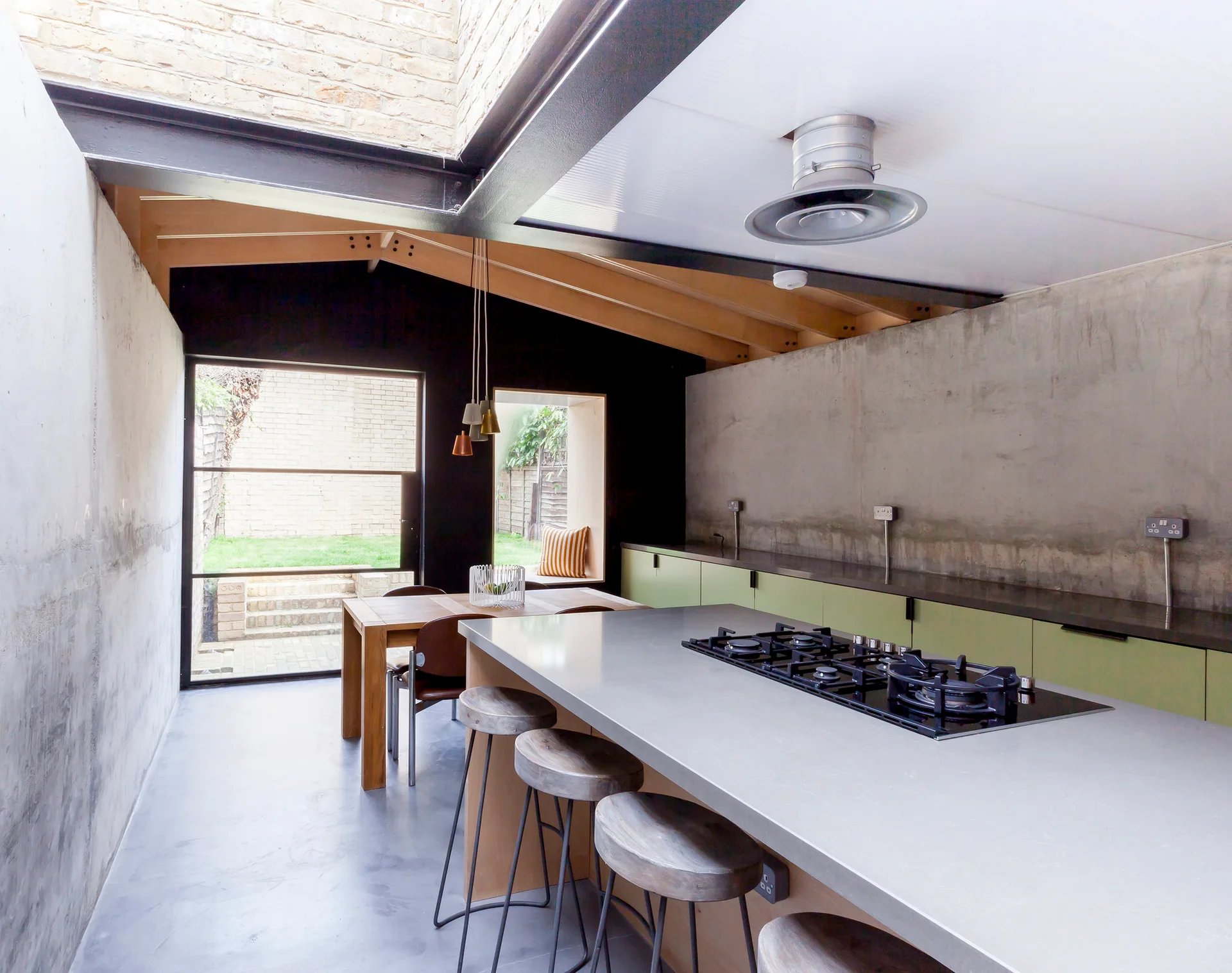 A modern industrial kitchen featuring exposed concrete walls, a large island with a gas cooktop, and olive green lower cabinets.