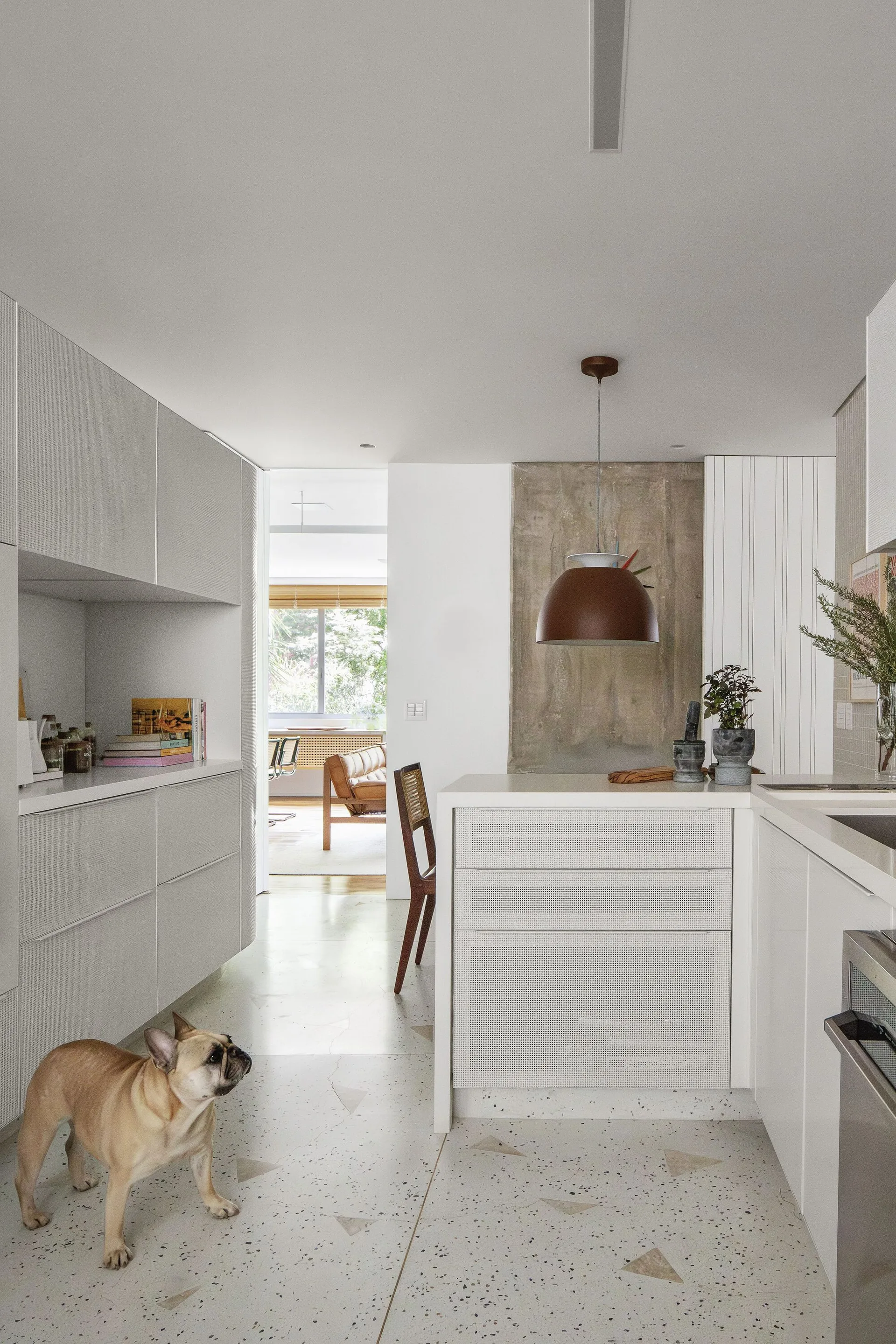 A modern white kitchen features perforated cabinet fronts, a light grey terrazzo floor with geometric inlays, and a brown dome pendant light.