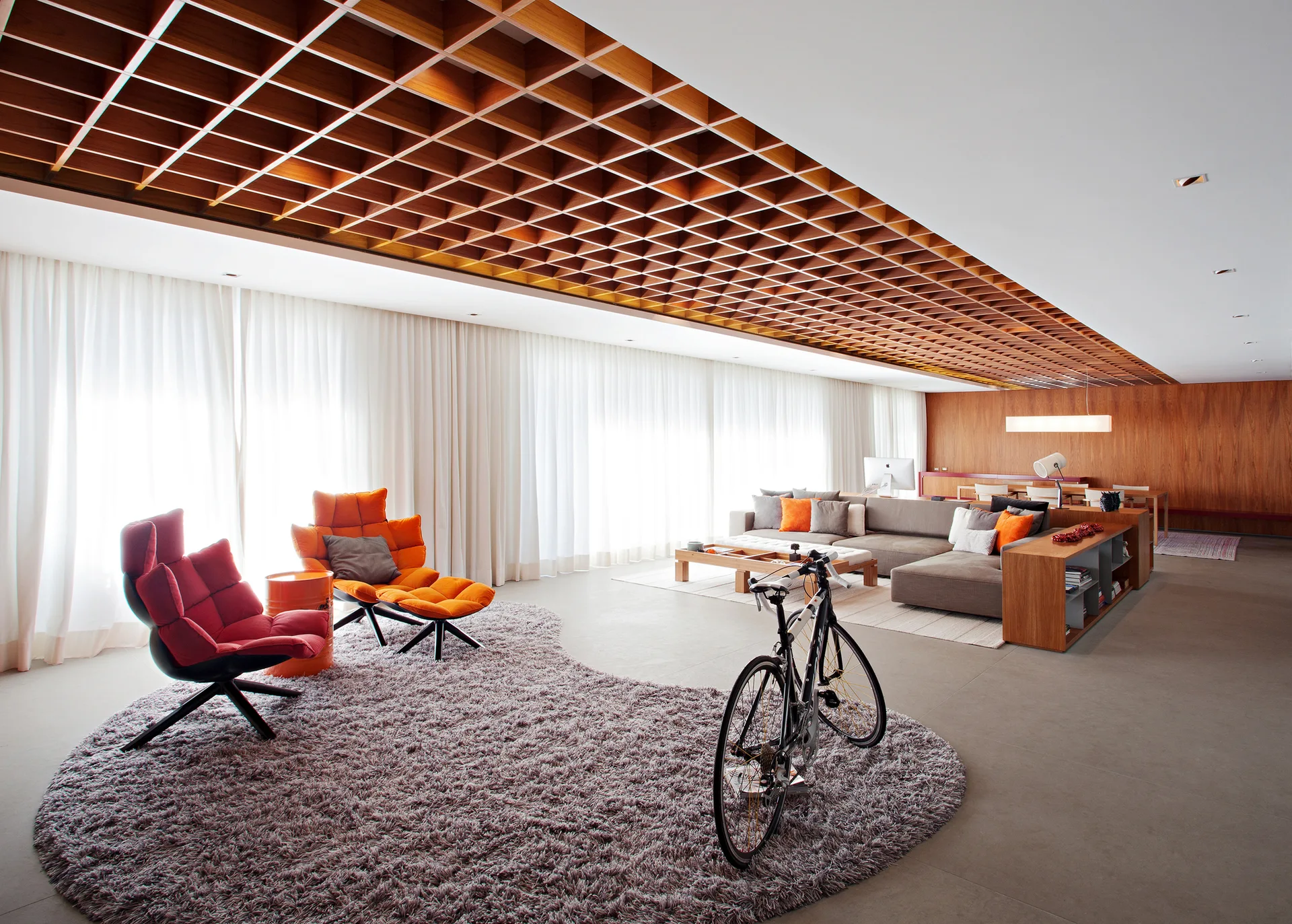 A modern living room features a wooden coffered ceiling, a large grey sectional, colorful accent chairs, and an irregular purple shag rug.