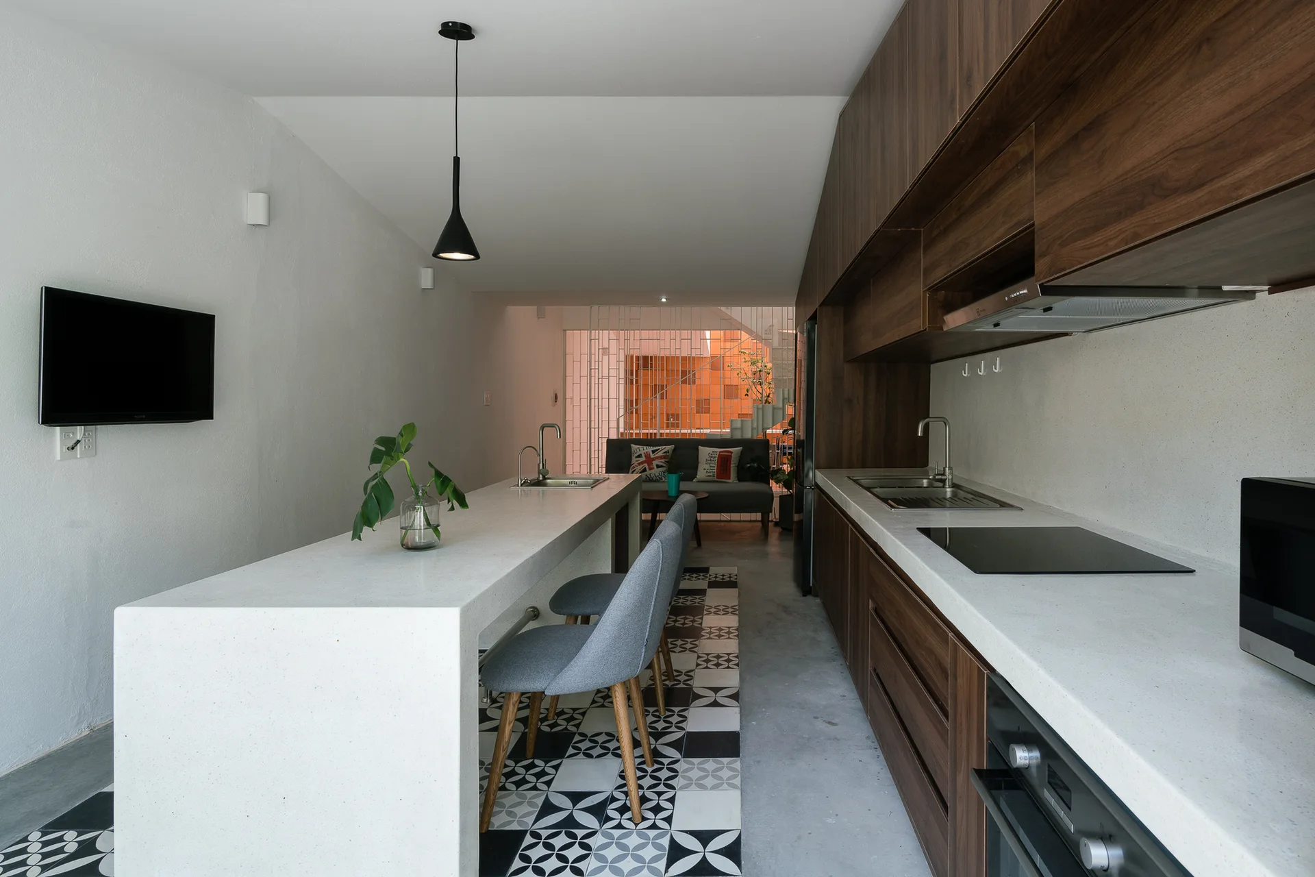 A modern kitchen features a long white stone island with gray stools set over a black and white geometric tile runner alongside wood-toned cabinets.