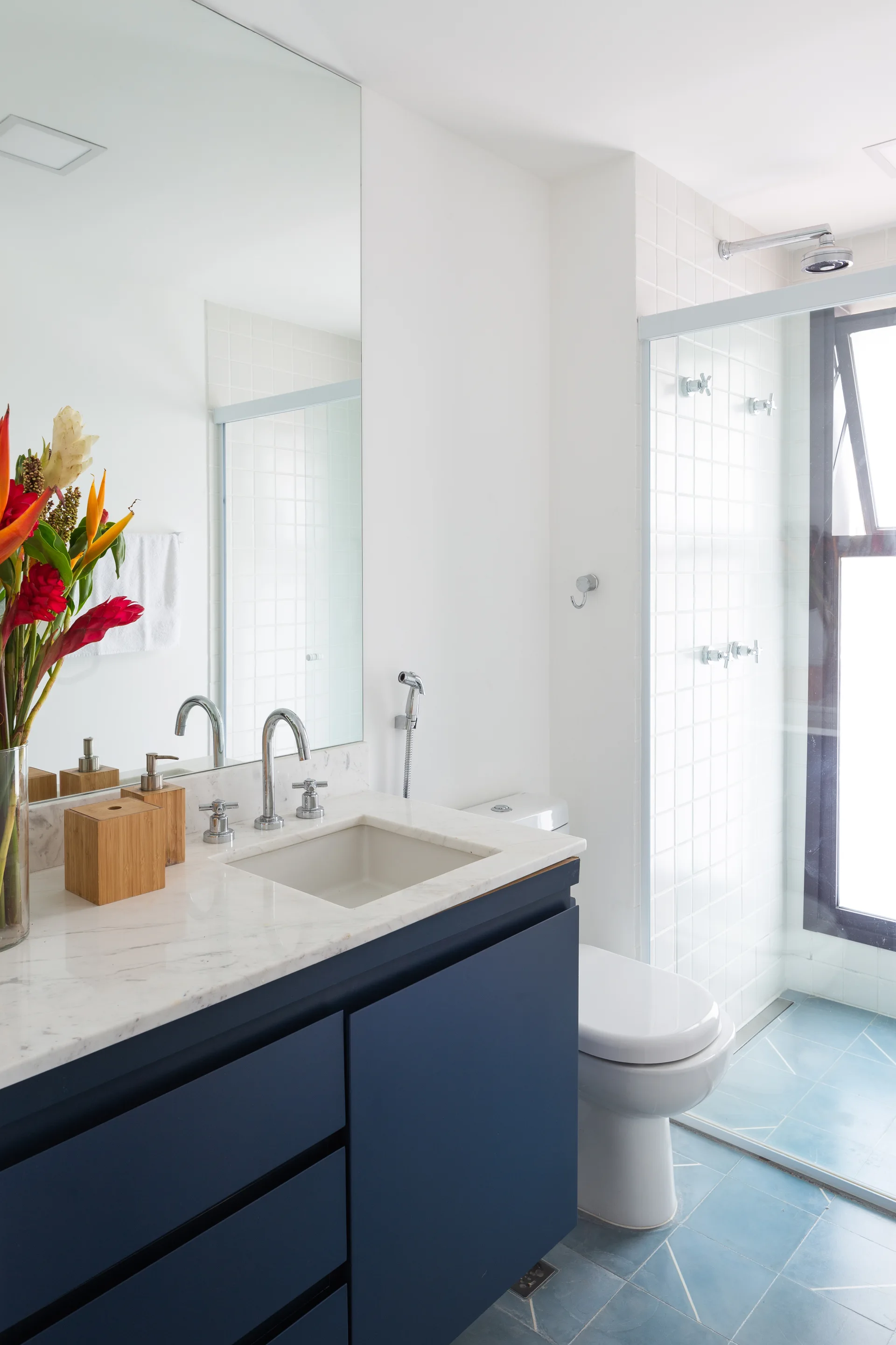 A modern white bathroom features a navy blue vanity with a marble countertop, a glass shower, and blue patterned floor tiles.