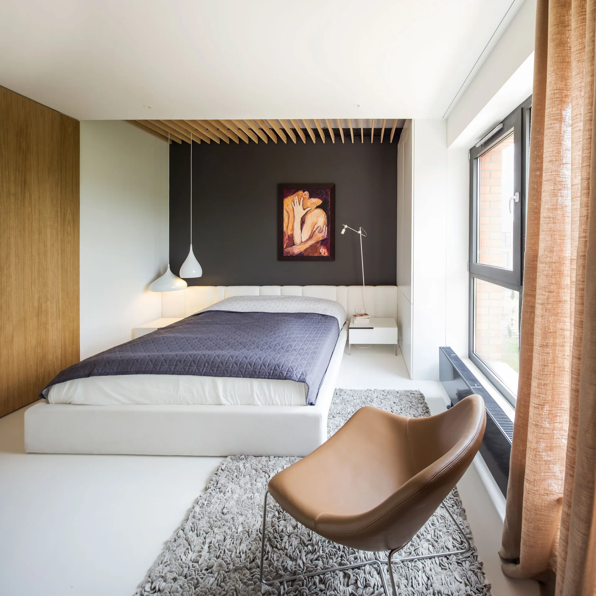 A modern bedroom features a low white platform bed against a dark feature wall, topped by a slatted wood ceiling insert and a shag rug.