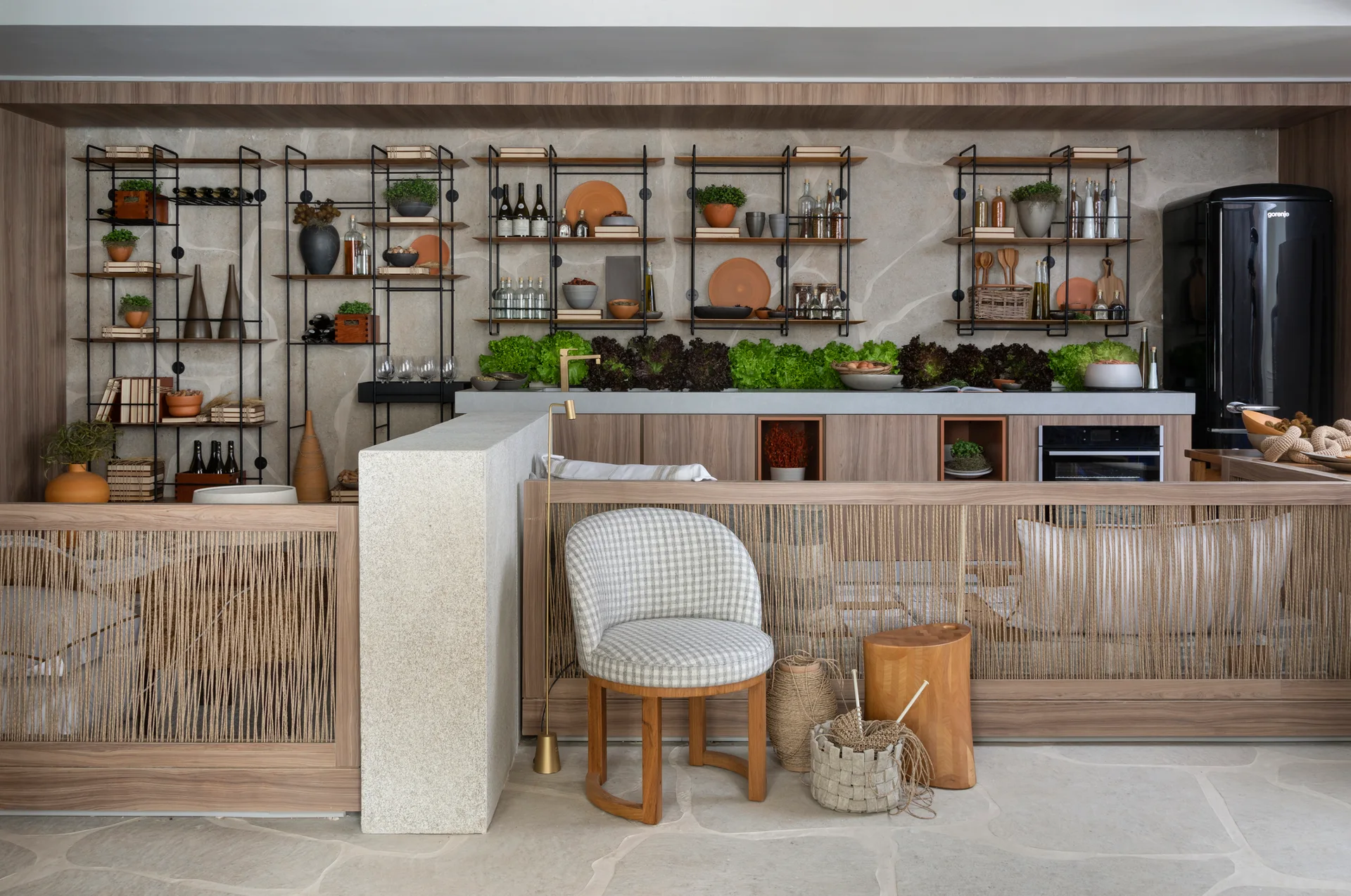 An organic modern kitchen features warm wood cabinetry, a beige stone wall, black metal open shelving, and a vertical rope partition screen.