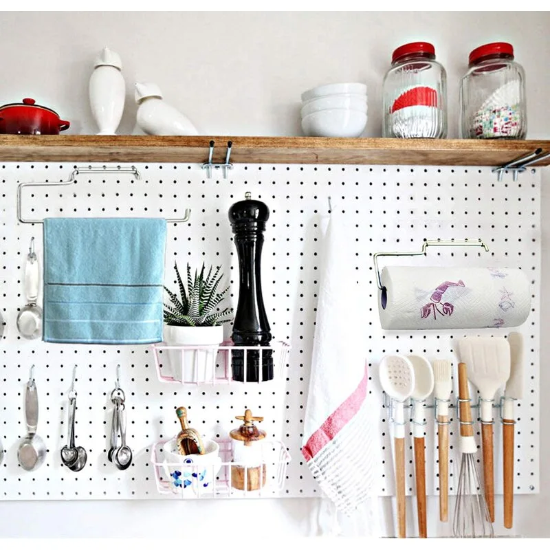A white kitchen pegboard organizer mounted below a wooden shelf displays hanging utensils, towels, wire baskets, and jars.