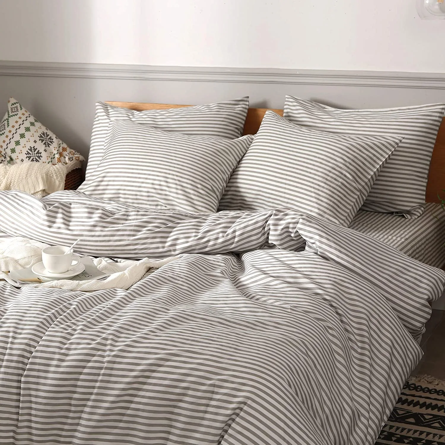 A bed is neatly made with a gray and white striped duvet, matching pillows, a textured throw blanket, and a white coffee cup on a small tray.