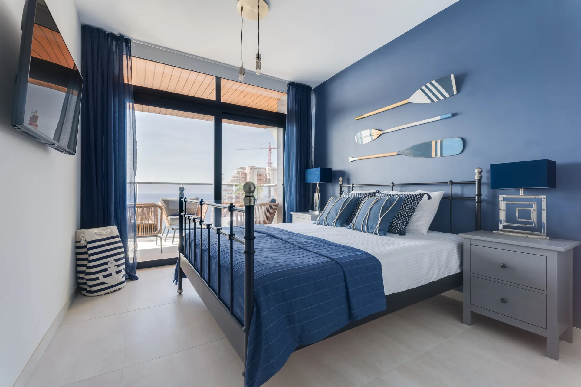 A nautical bedroom featuring a black metal bed set against a dark blue accent wall decorated with three hanging oars.