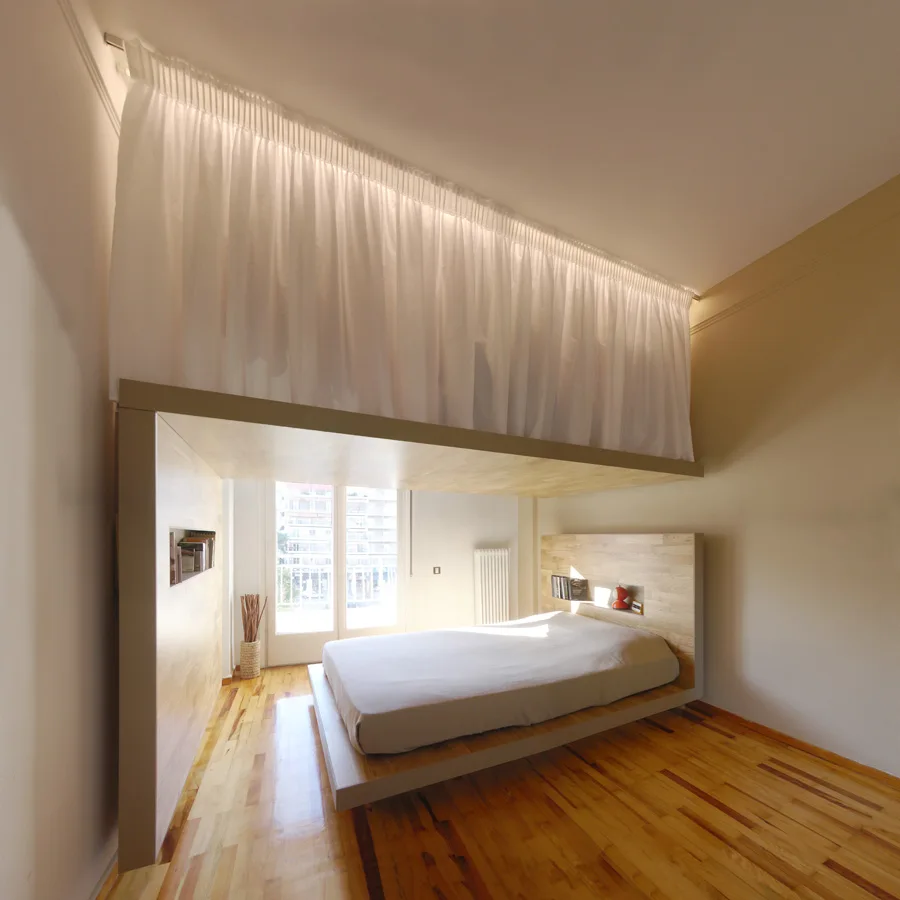A low wooden platform bed is integrated into a light wood canopy structure beneath a white curtain partition hanging from the ceiling.
