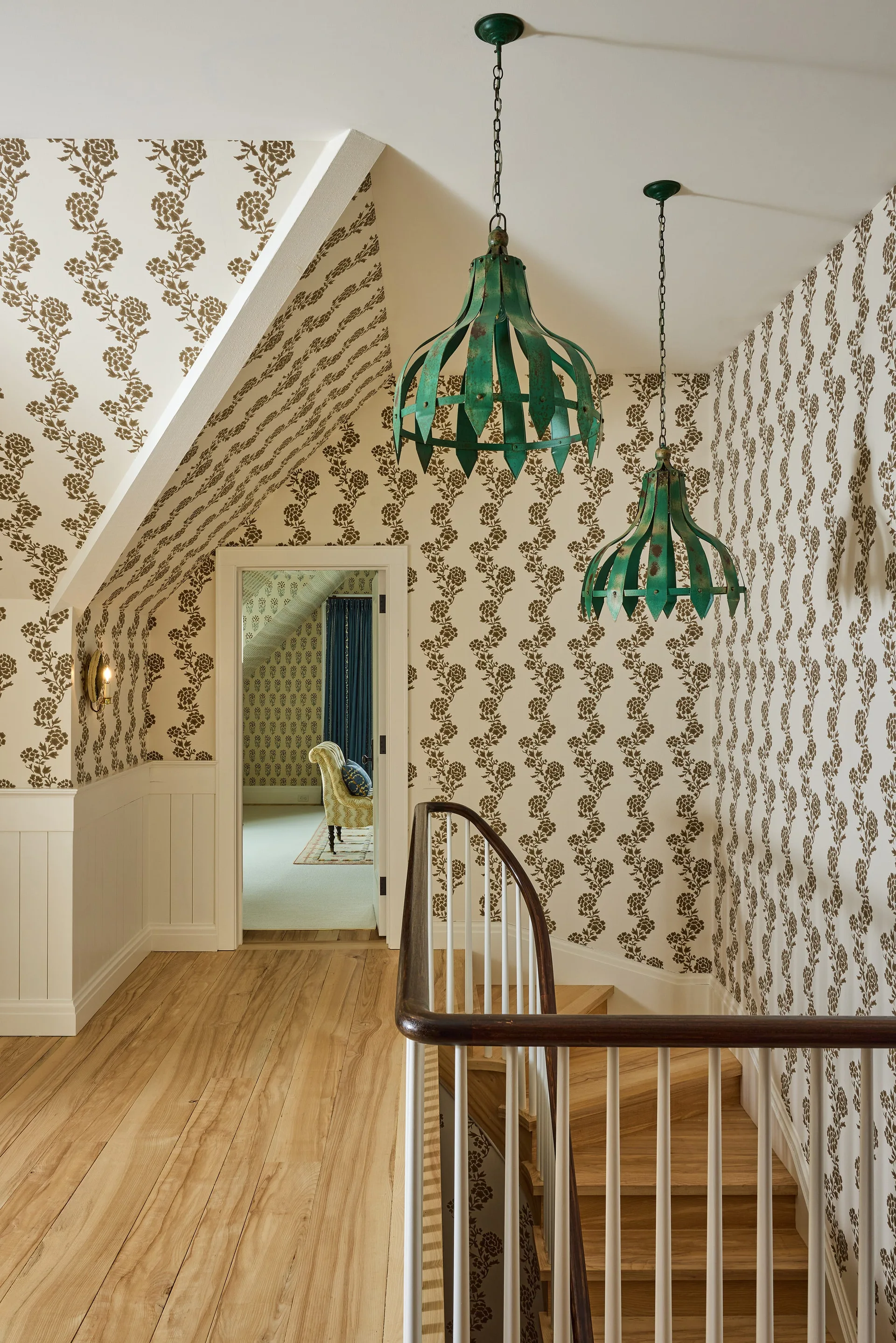 A traditional staircase landing featuring brown and white floral wallpaper, white beadboard wainscoting, and green metal pendant lights.