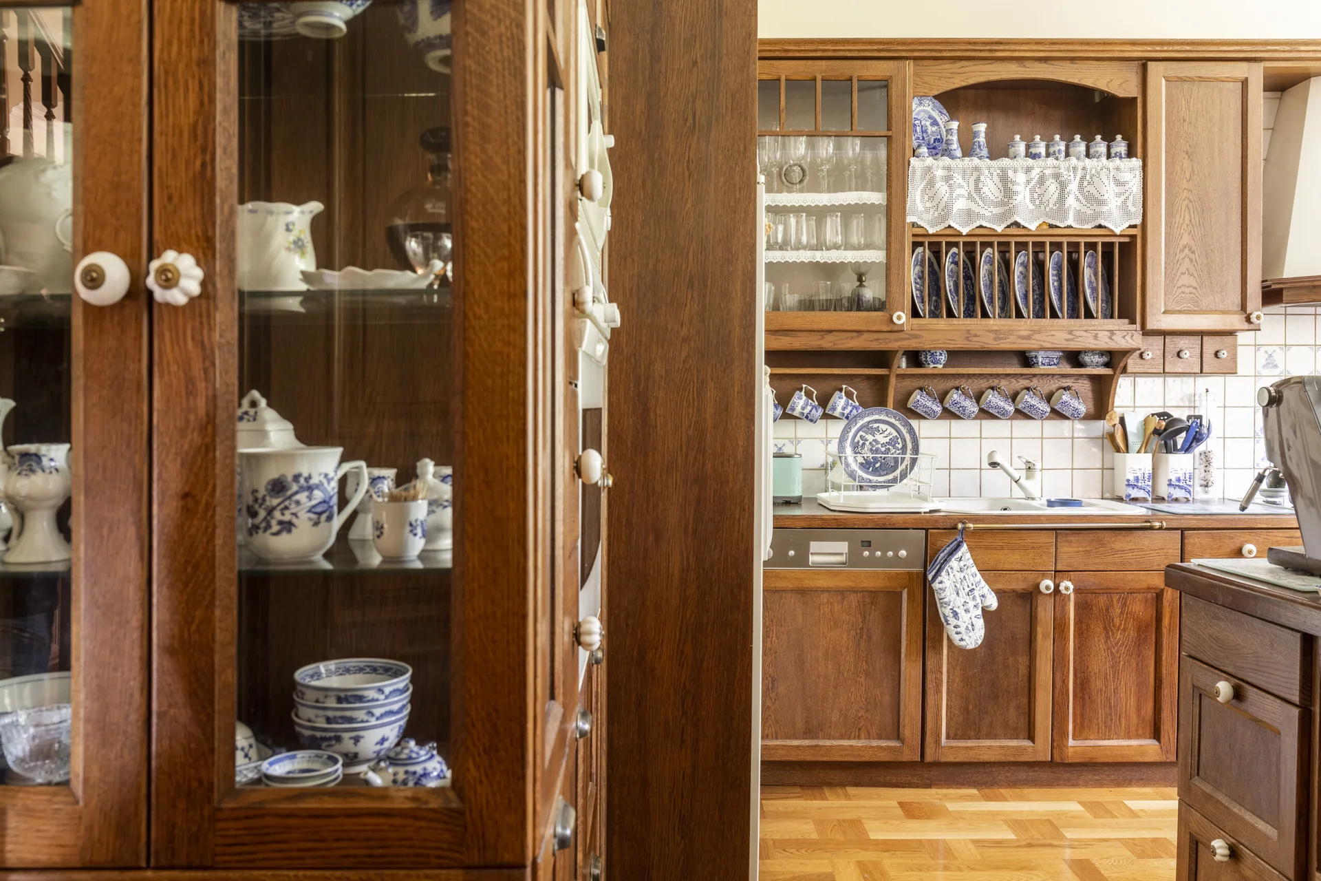 A traditional kitchen features warm wood cabinetry with glass doors, a wall-mounted plate rack, and blue and white patterned porcelain dishes.