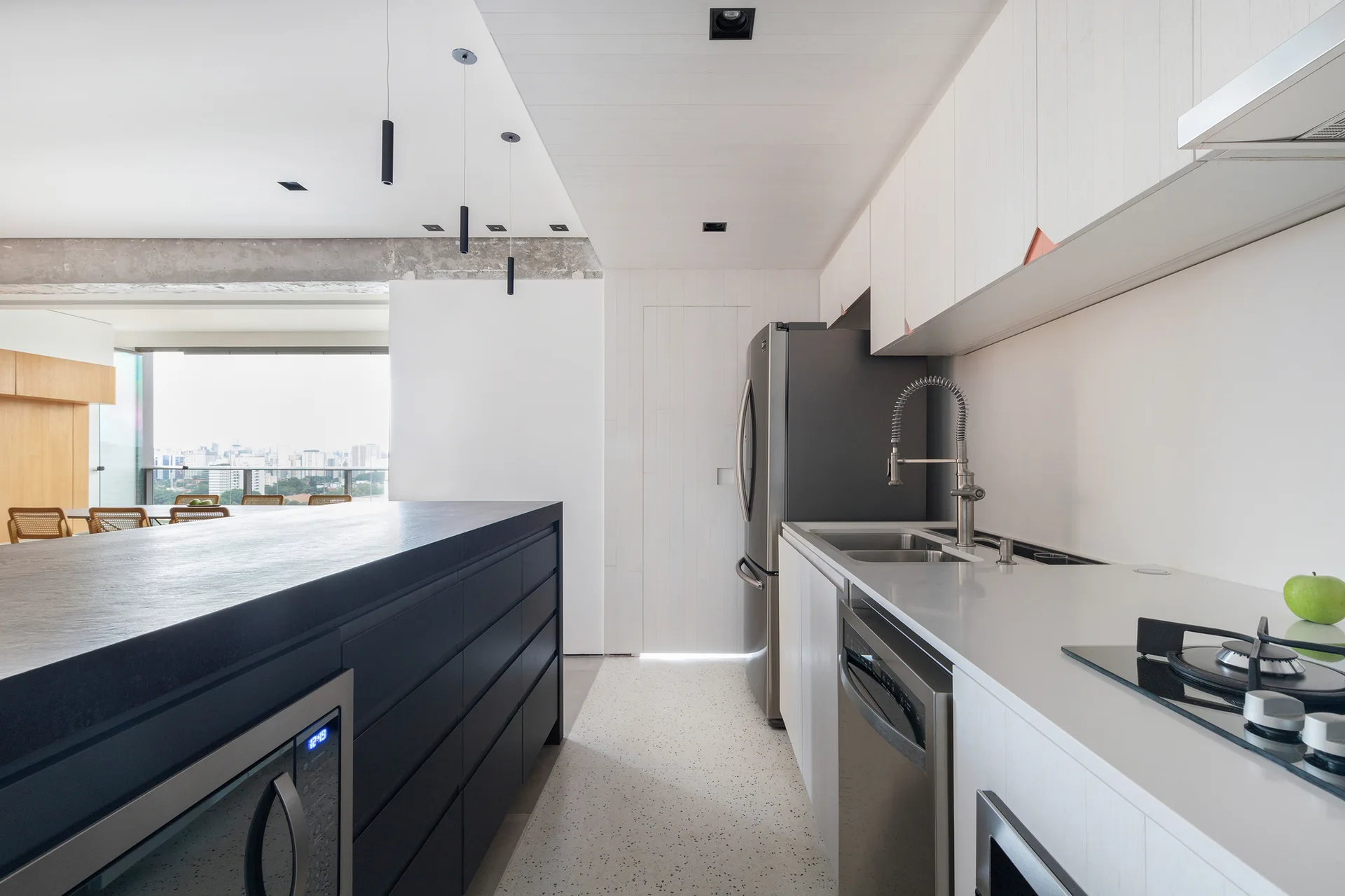 A modern kitchen with a dark-topped black island, white wood-grain cabinets, stainless steel appliances, and a raw concrete ceiling beam.