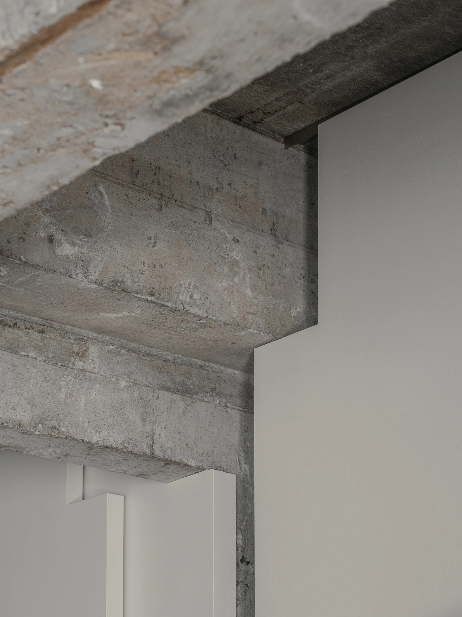 A detailed view of a textured grey concrete structural beam joining a smooth matte white interior wall panel.