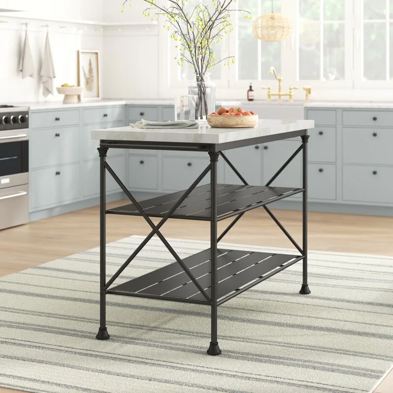 A freestanding black metal kitchen island with a white marble top sits on a striped rug in front of pale blue shaker cabinets.