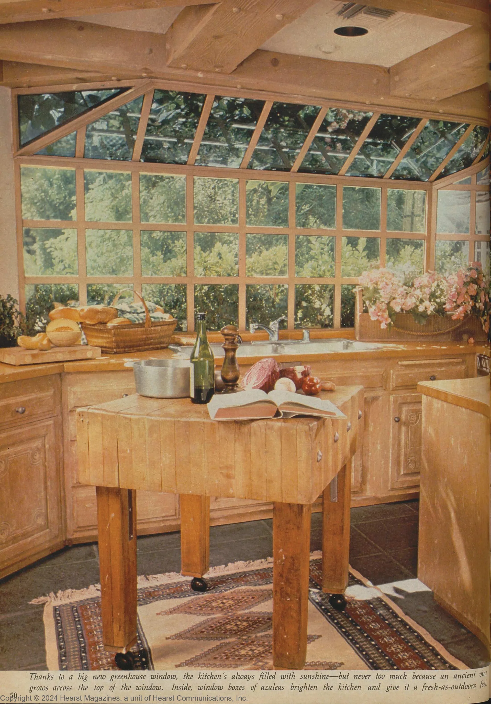 A rustic kitchen features a central wooden butcher block island on a geometric rug beneath a large multi-pane greenhouse window.