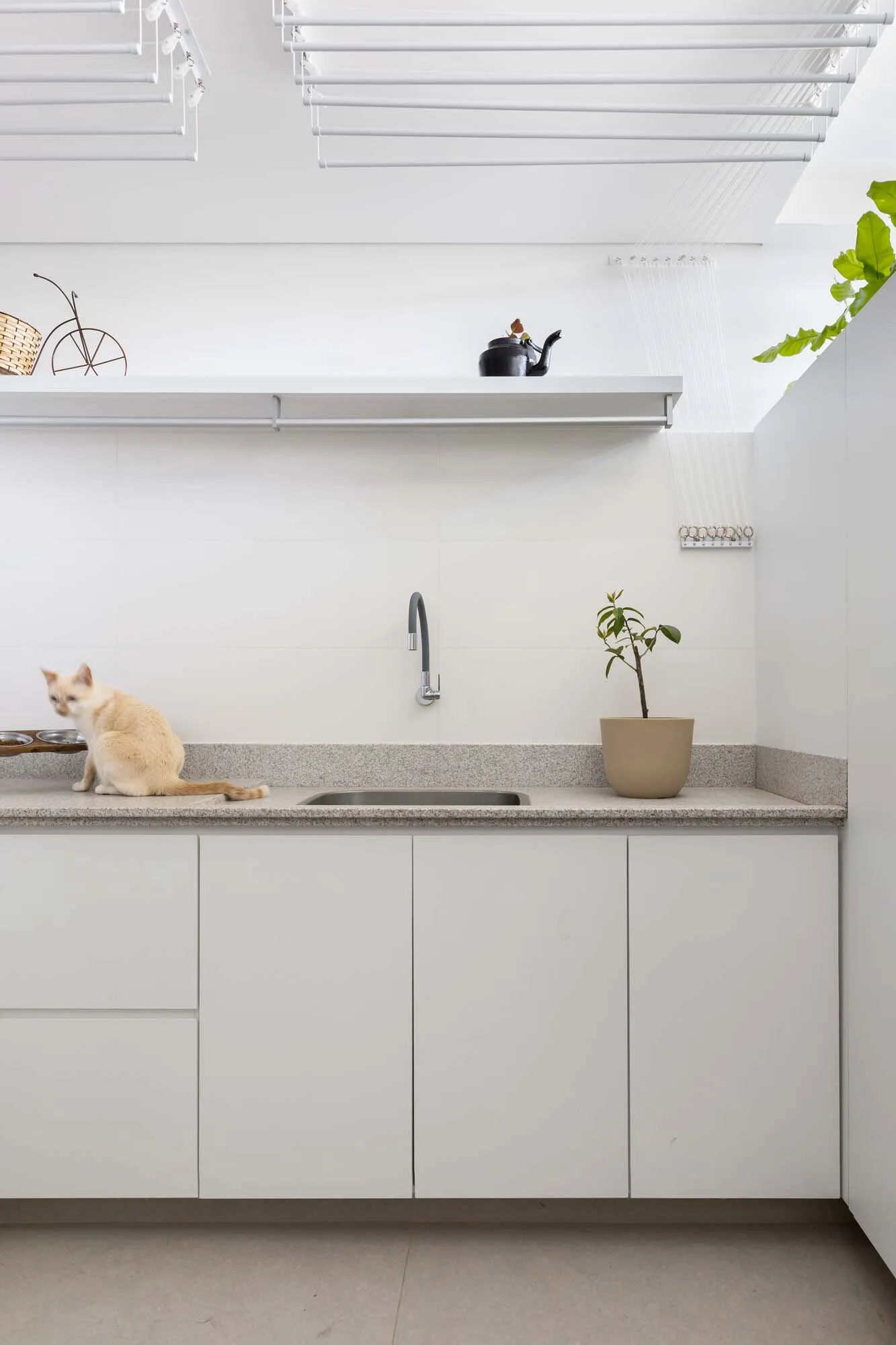 A minimalist white utility kitchen features flat-panel cabinets, a grey speckled stone countertop with a sink, and a white ceiling-mounted drying rack.