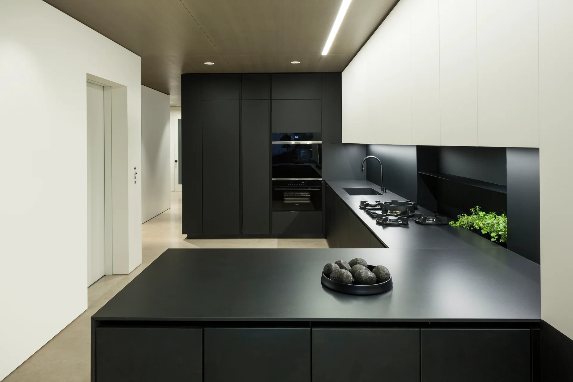 A minimalist kitchen featuring matte black lower cabinets, white upper cabinetry, and a wood paneled ceiling with linear recessed lighting.