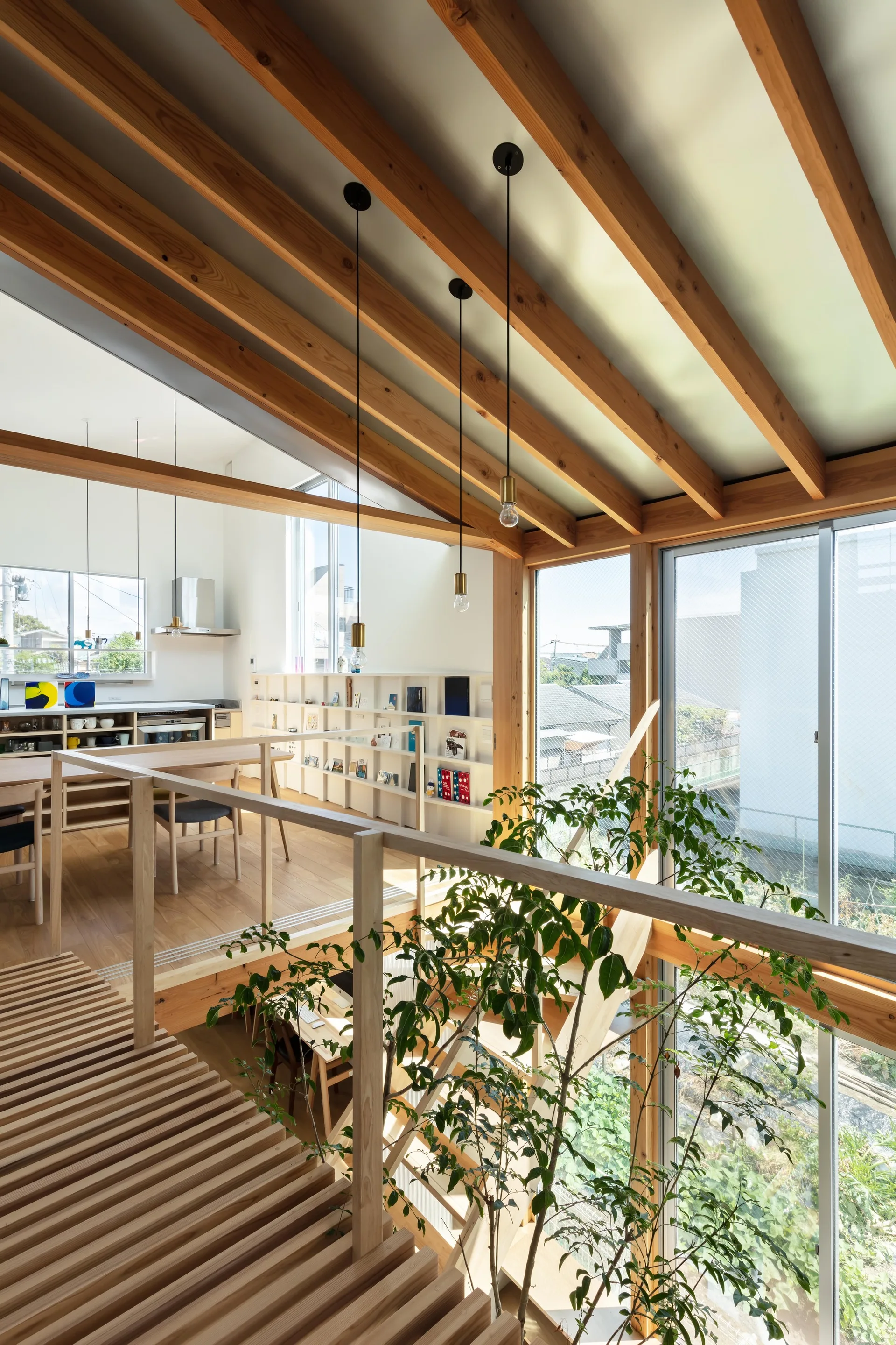 An open-plan loft interior with exposed timber ceiling beams, a light wood slatted staircase, and white built-in bookshelves.