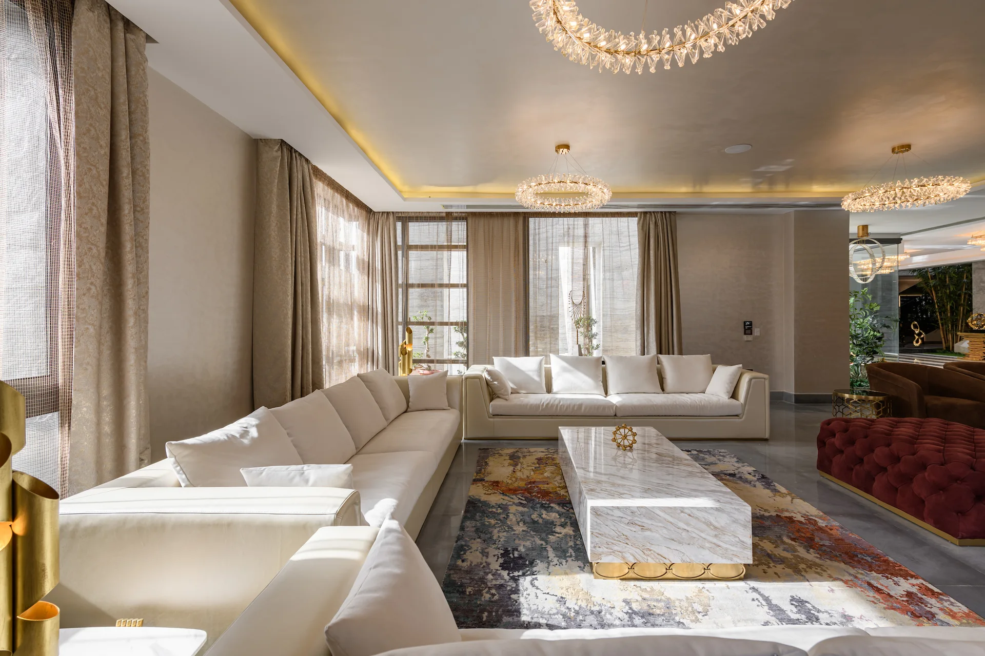 A spacious living room features two large white sectional sofas arranged around a long marble coffee table on an abstract patterned area rug.
