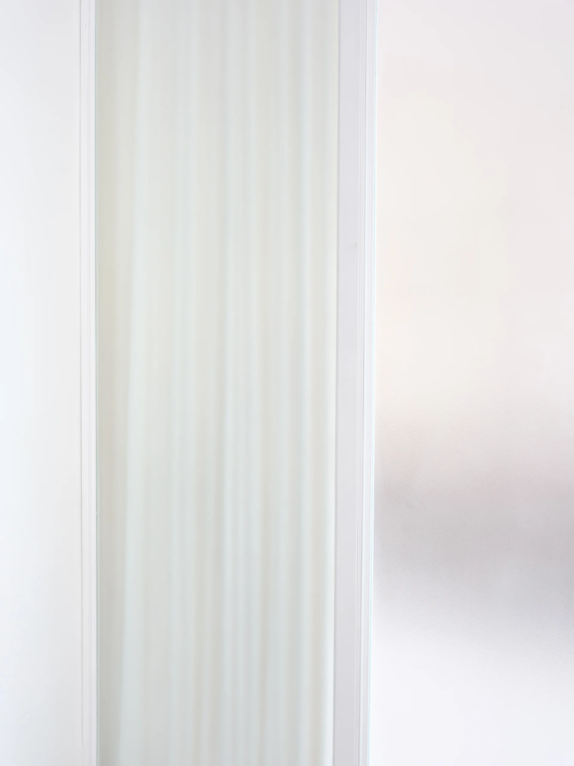 A close-up view of a minimalist white interior door featuring a vertical recessed panel and clean painted trim.