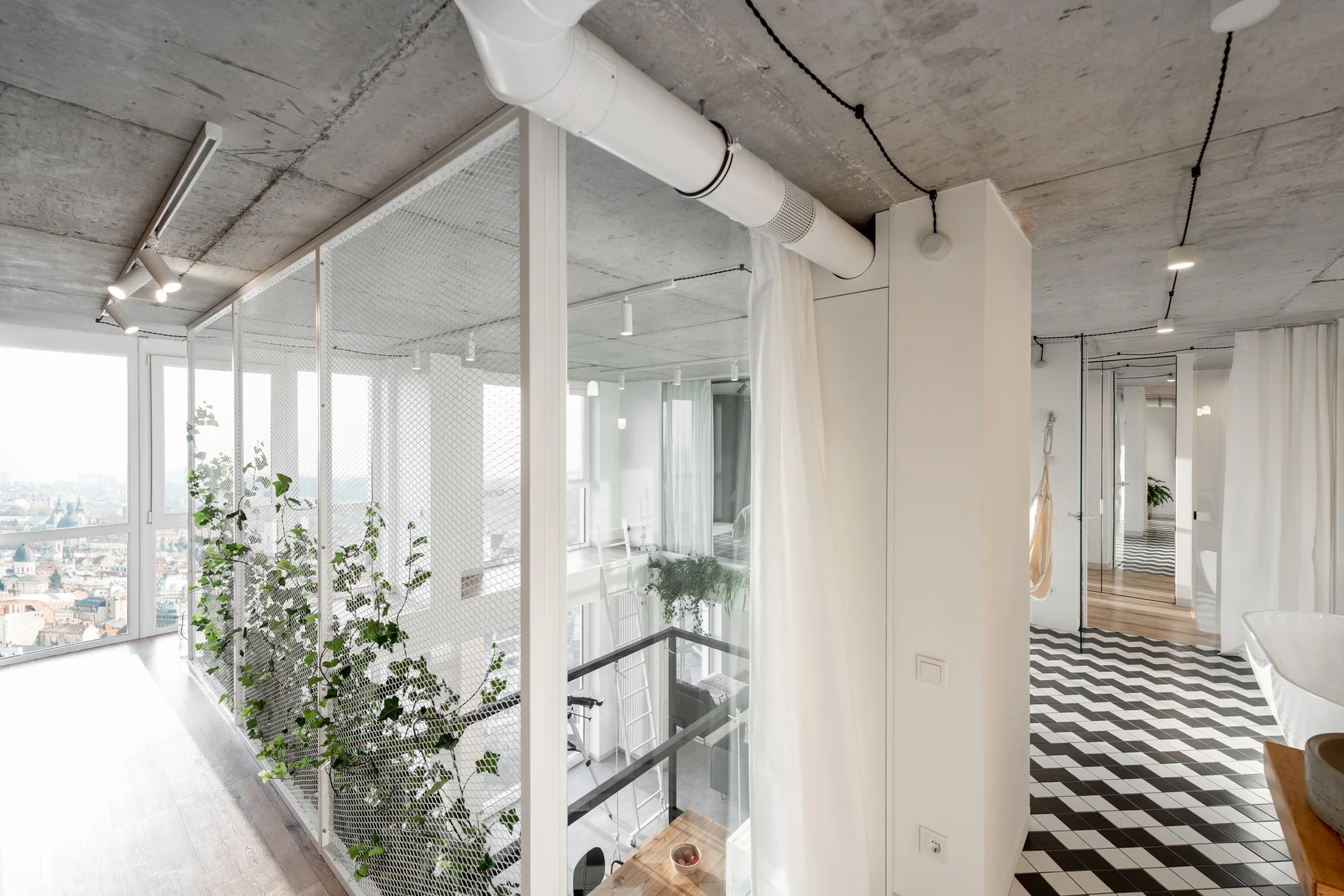 A modern apartment loft features an exposed concrete ceiling, a white mesh divider covered in climbing vines, and a checkered tiled floor.