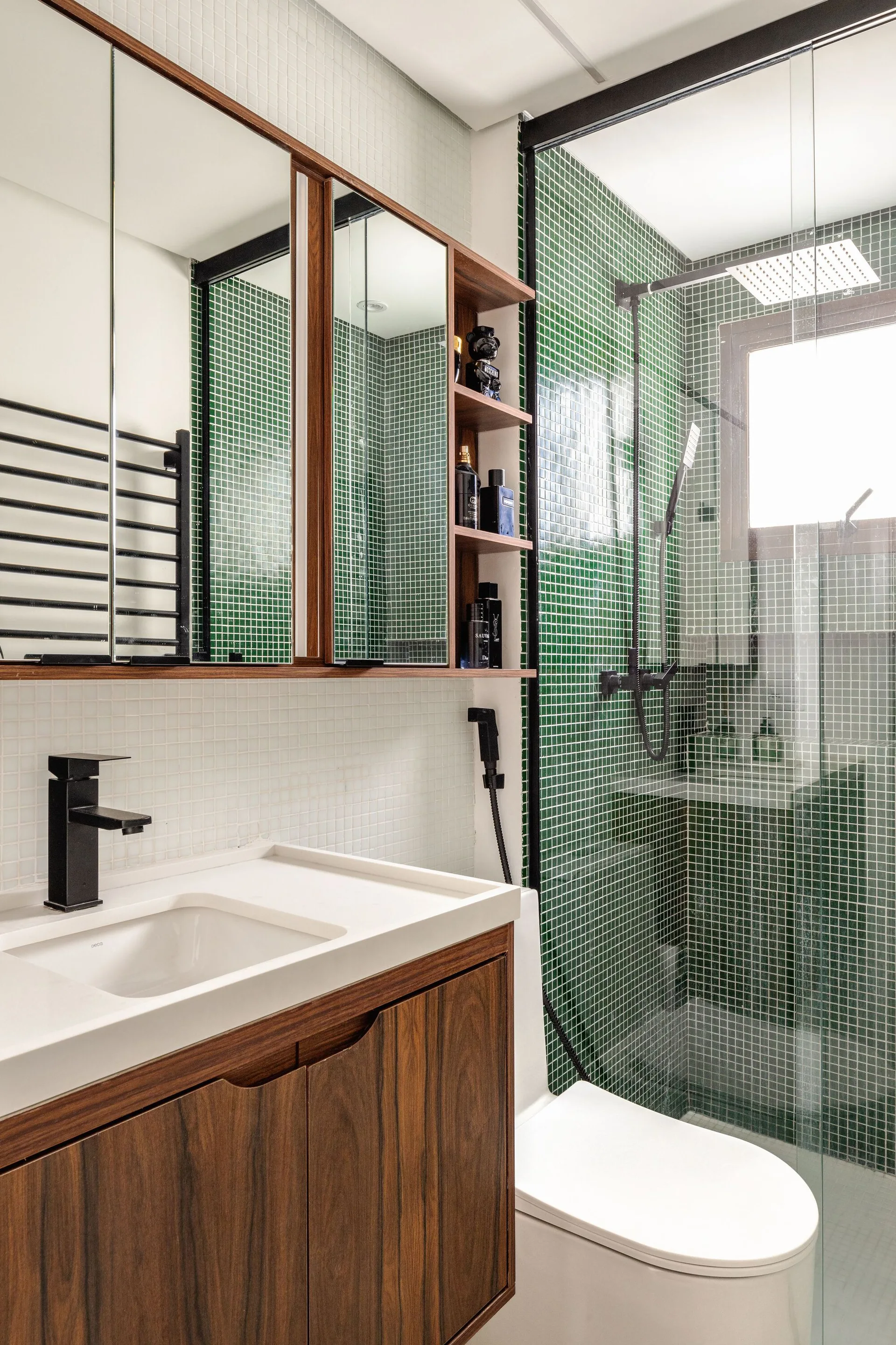 A modern bathroom featuring a wood grain vanity, white sink, matte black faucet, and a walk-in shower with green mosaic tile walls.