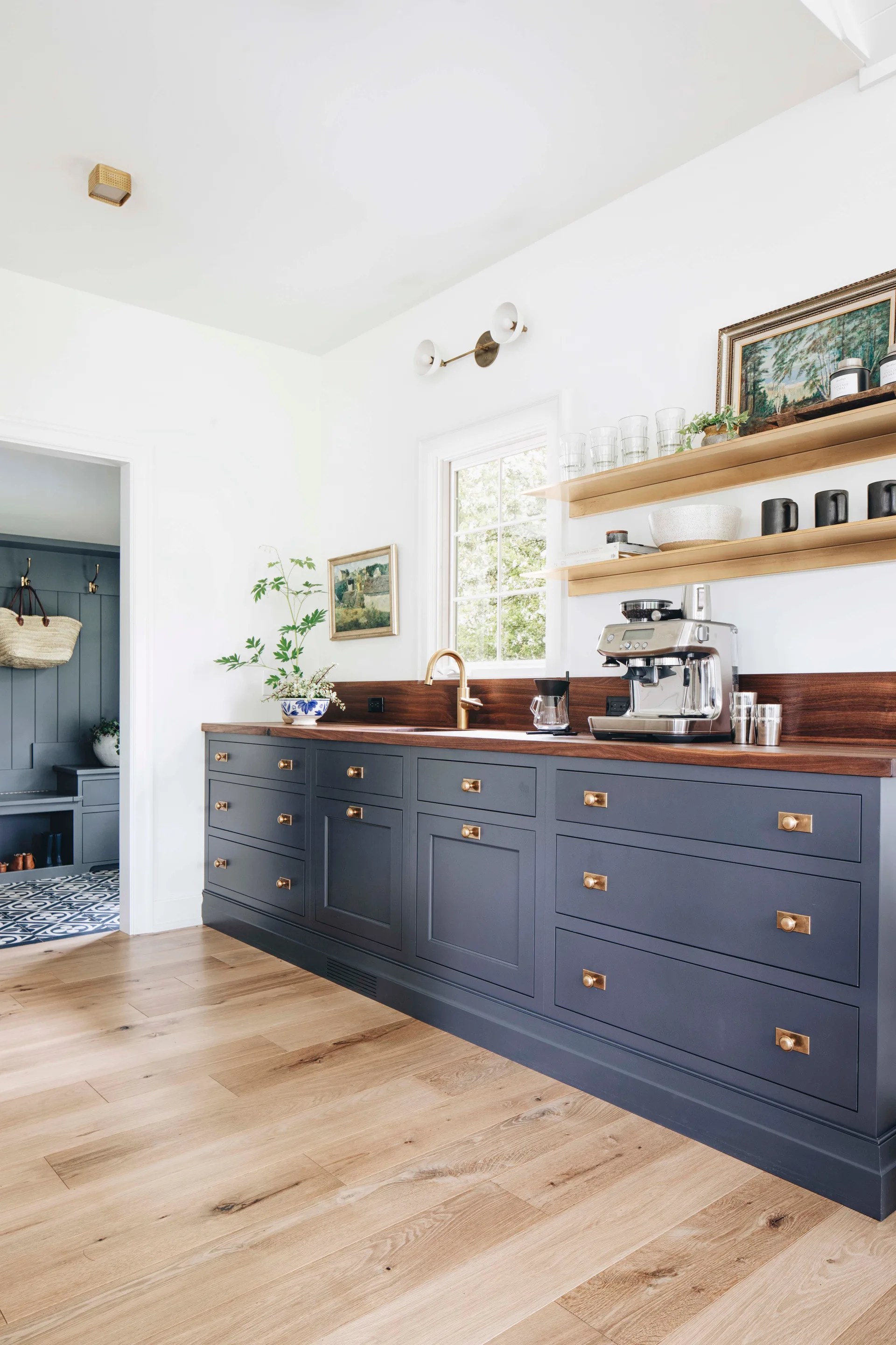 Navy blue kitchen base cabinets with brass hardware, a dark wood countertop, and matching floating shelves on a white wall.