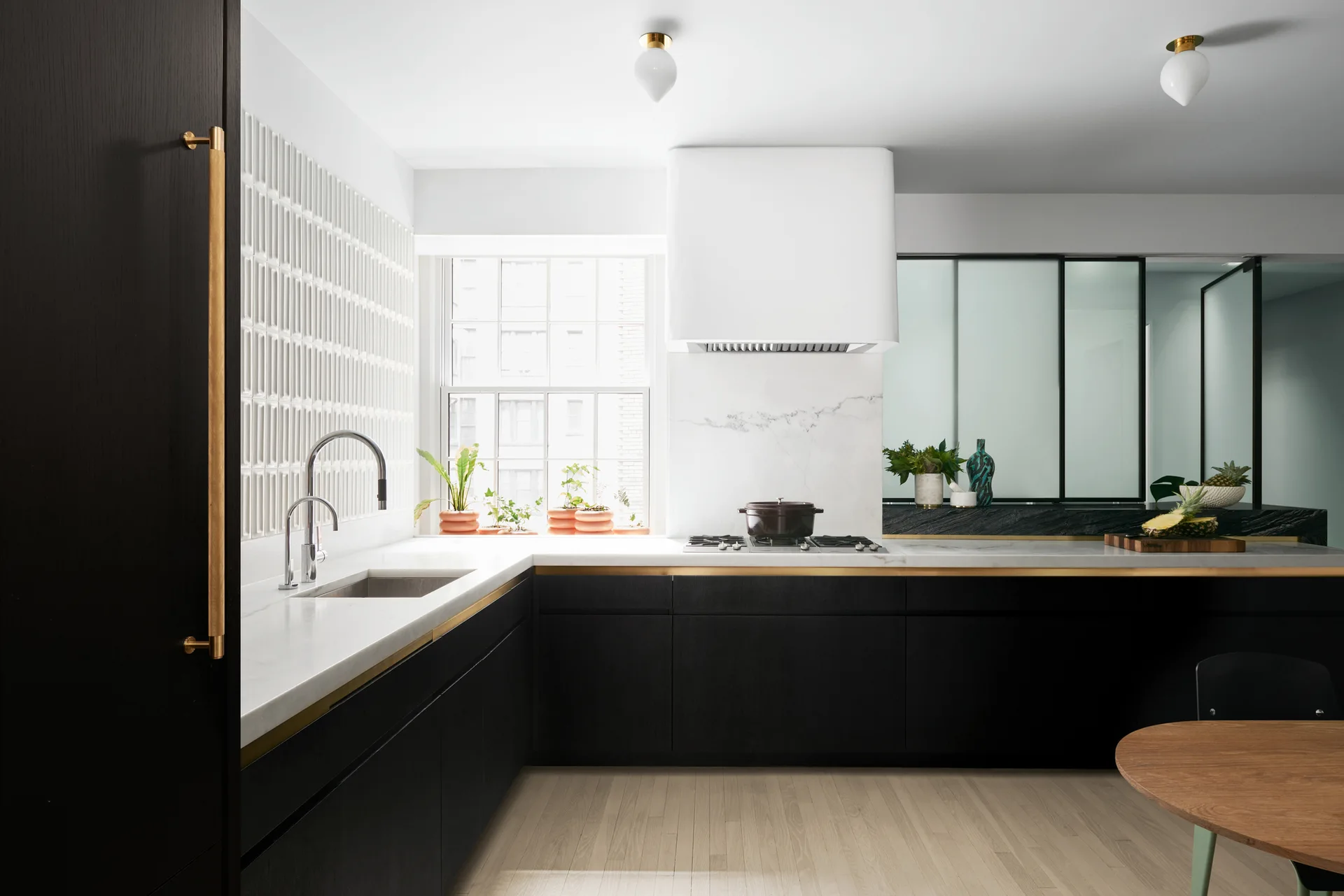 A modern kitchen features matte black base cabinets with brass trim, white stone countertops, a white range hood, and vertical tile backsplash.