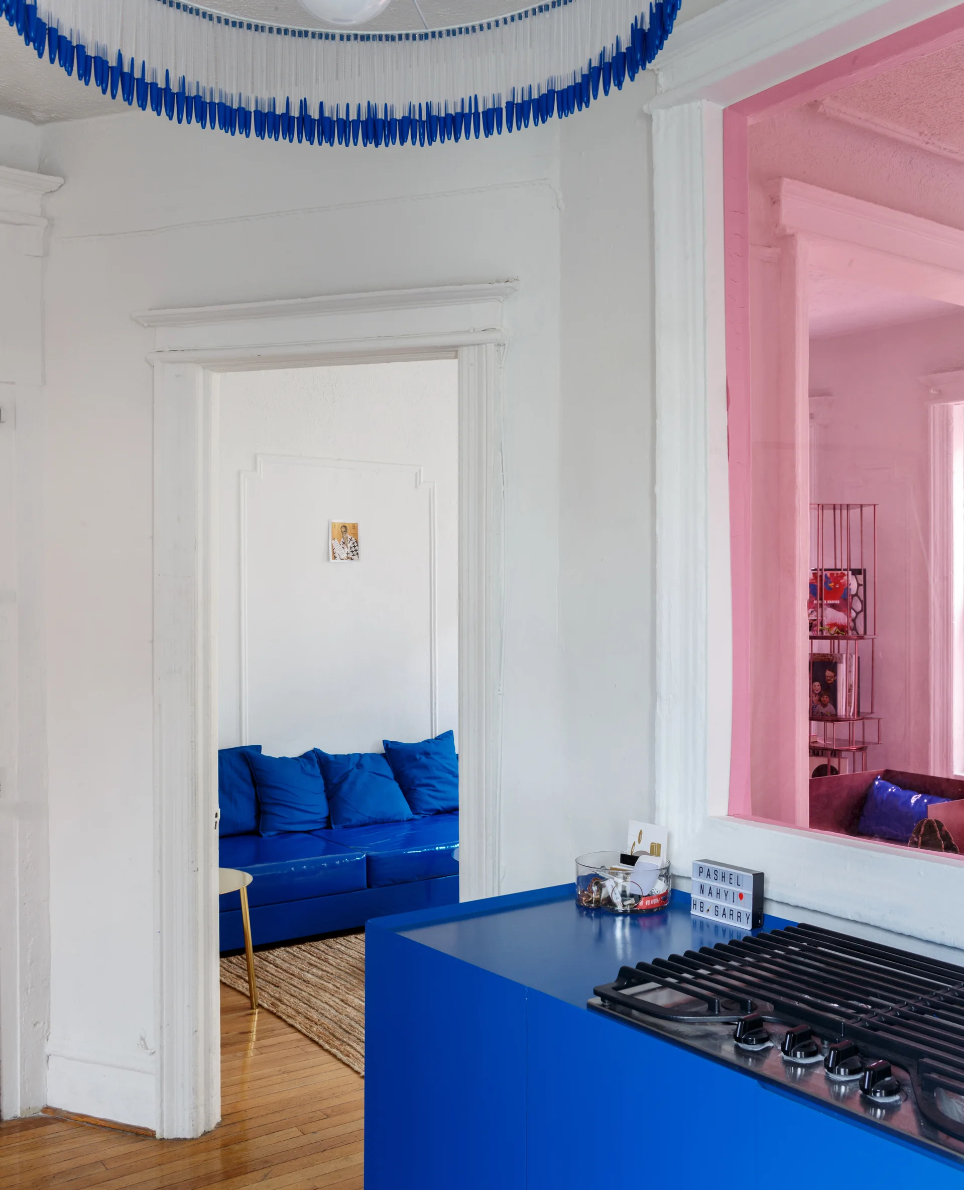 A bright blue kitchen island with a gas stovetop looks through a white doorway toward a matching blue sofa on a jute rug.