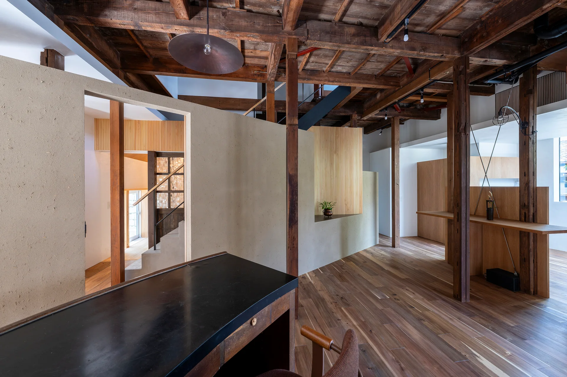 An open interior space featuring exposed dark wood ceiling beams, textured tan partition walls, and warm wood flooring.