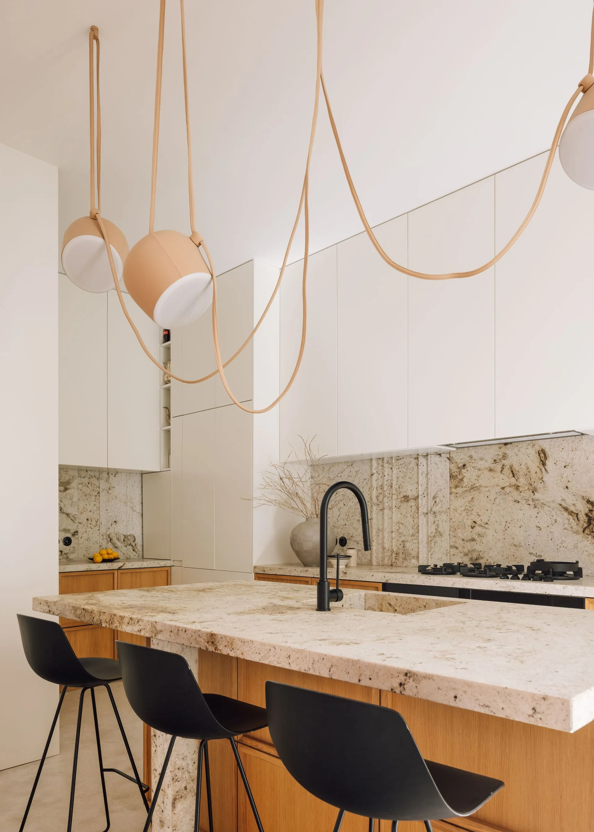 A modern kitchen features a speckled stone island with black bar stools, white flat-panel upper cabinets, and looped pendant lighting.