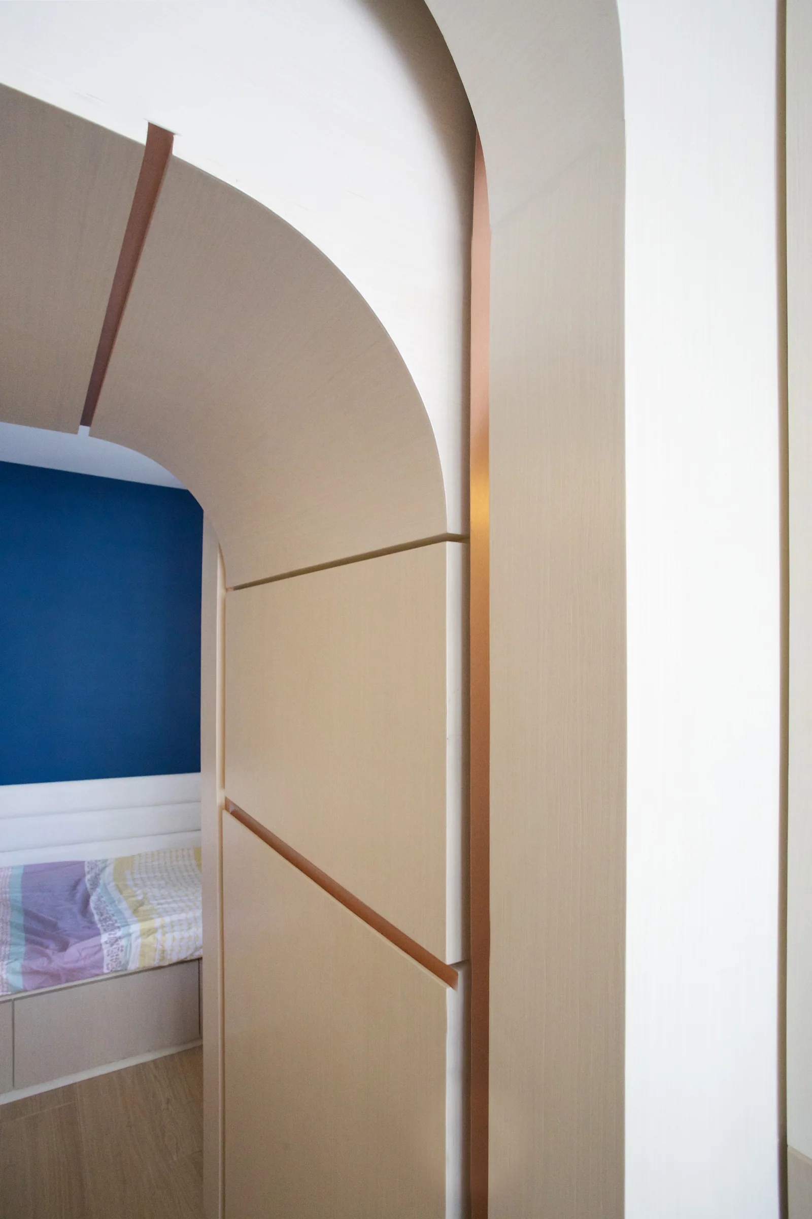 A light wood paneled archway with copper trim details frames a view into a bedroom featuring a deep blue accent wall.
