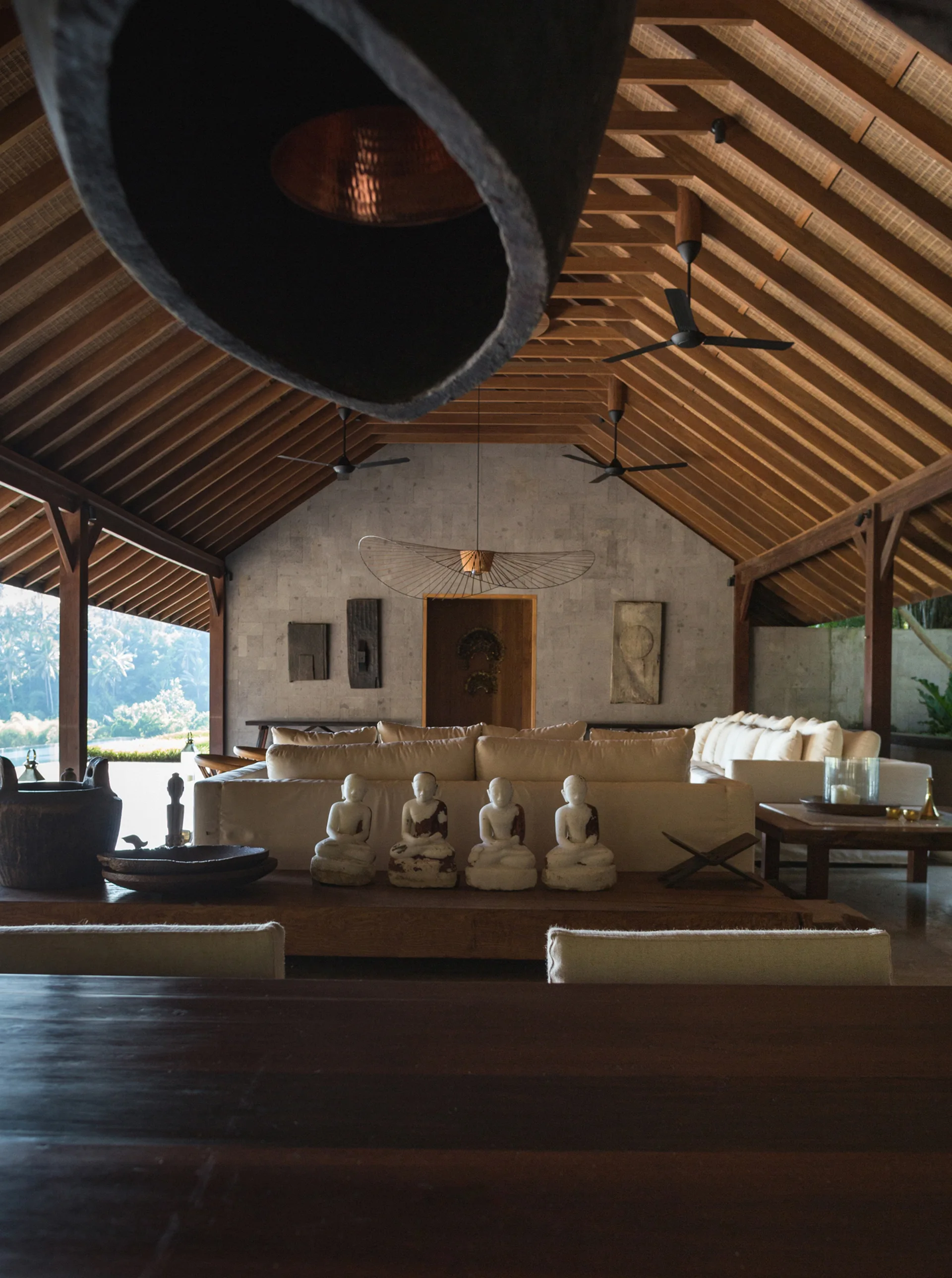 An open living space featuring a high vaulted wood ceiling, cream sofas, and a grey stone block wall decorated with small statues.