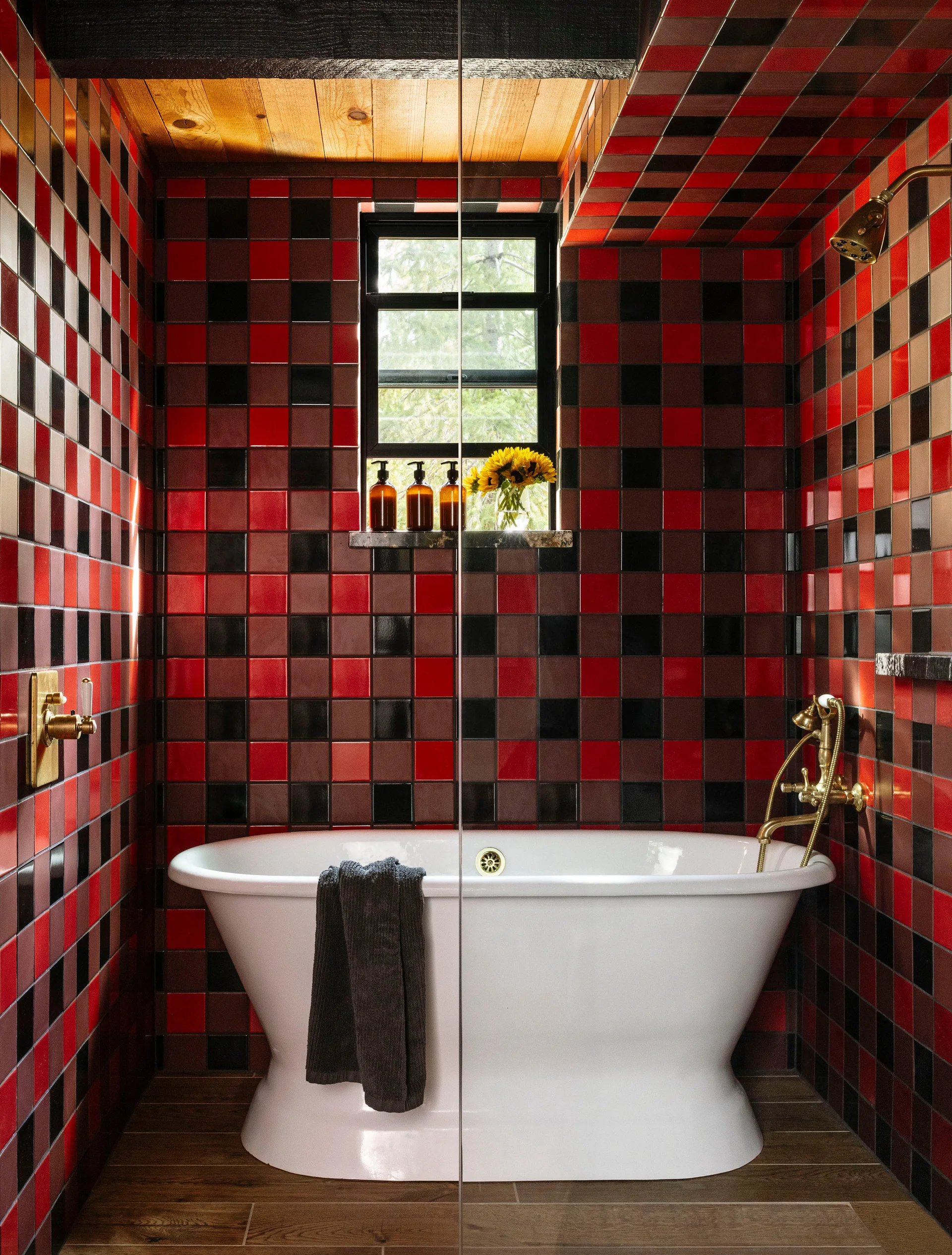 A white freestanding bathtub is centered against a bathroom wall clad in a bold red, black, and brown checkered tile pattern.