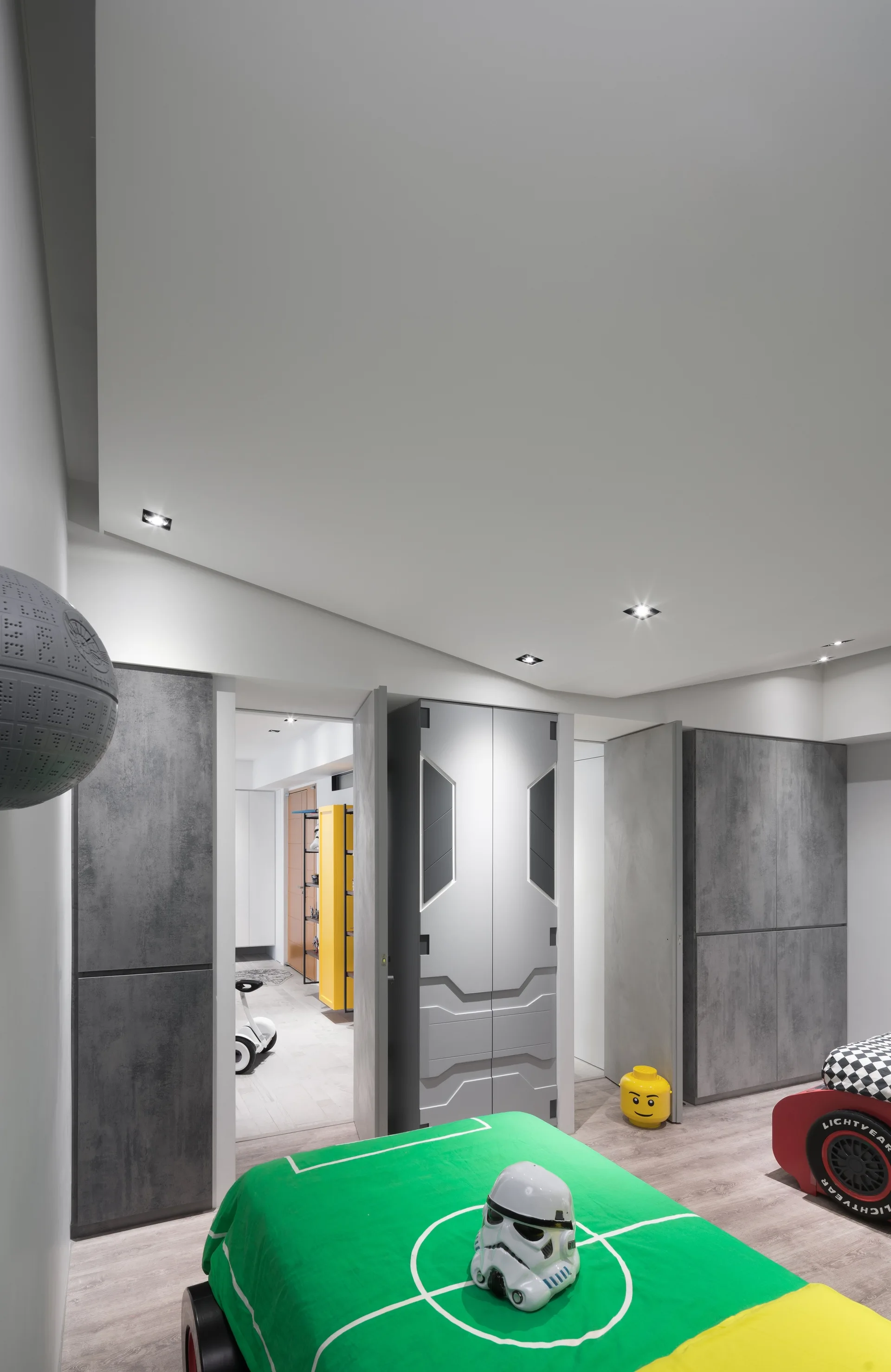 A kids bedroom features grey built-in wardrobes with geometric patterns, a green soccer-themed bed, and sci-fi themed wall decor.