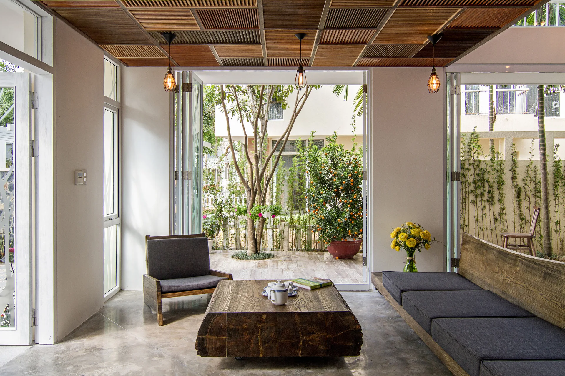 A living room features a slatted wood ceiling, a log coffee table, a grey sofa, and folding glass doors that open to a garden patio.