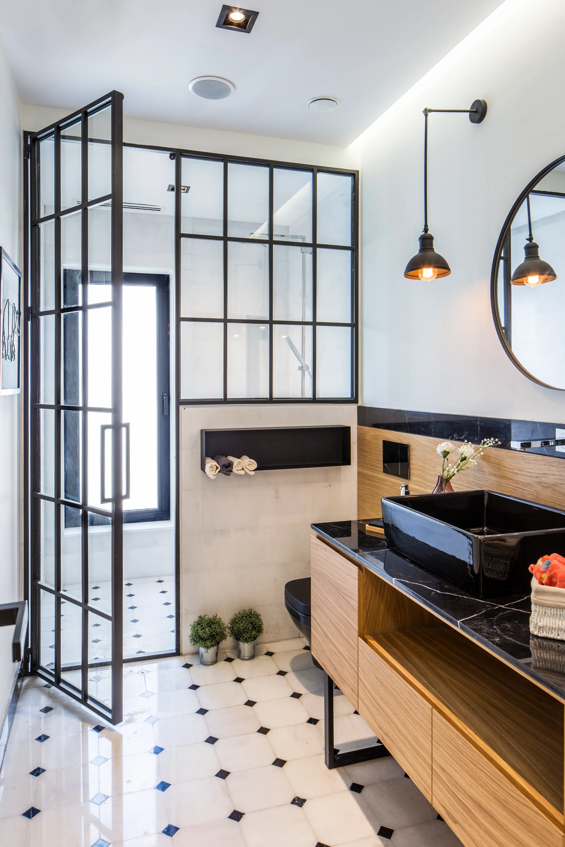 A modern bathroom with a black-framed glass shower partition, a light wood floating vanity, and a black vessel sink.