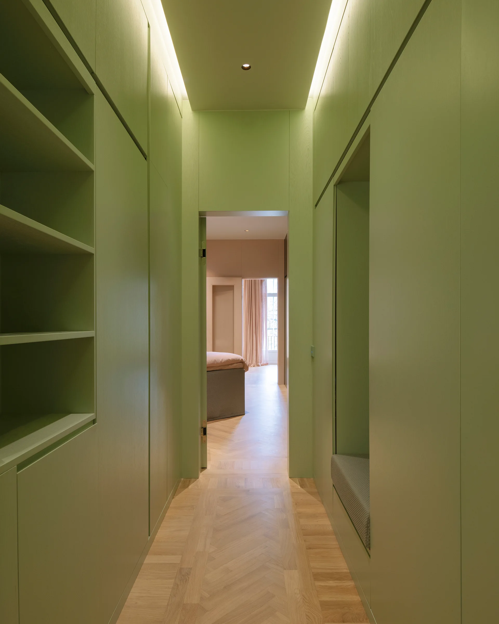 A narrow hallway features custom sage green built-in cabinetry, a recessed seating bench, parquet wood flooring, and hidden ceiling cove lighting.