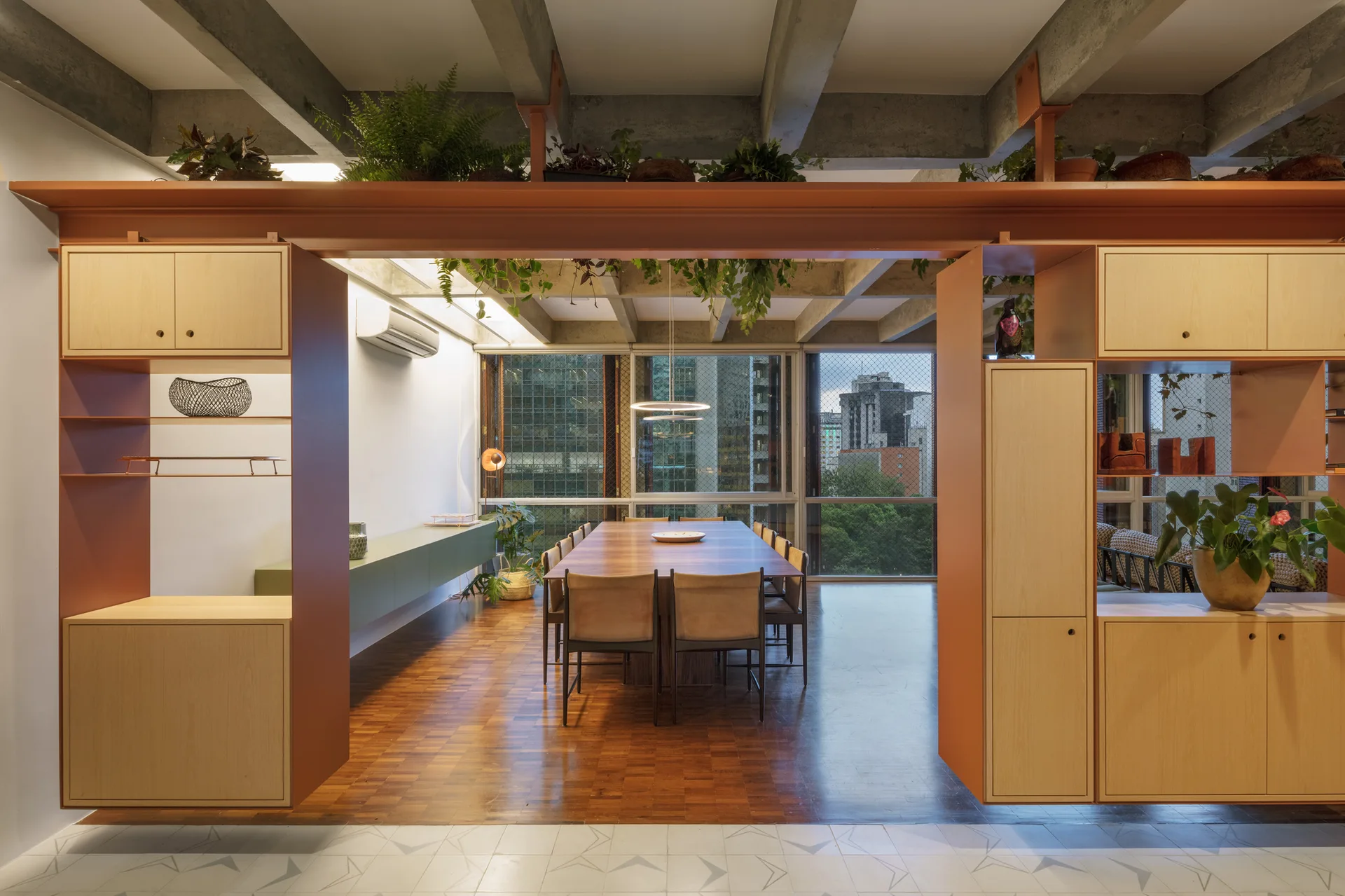 A modern dining room framed by a wood and terracotta room divider features a long wooden table beneath an exposed concrete ceiling.