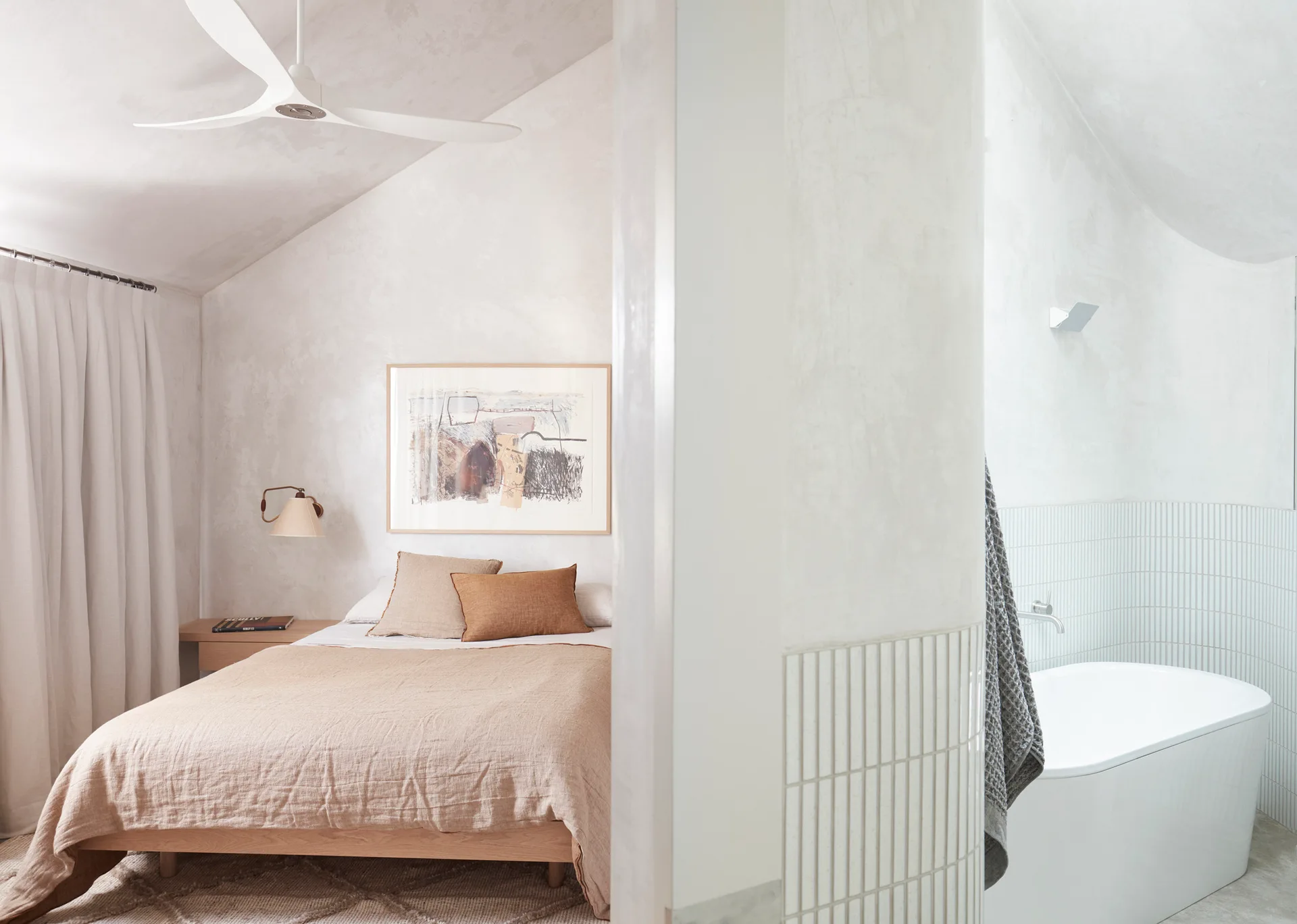A modern minimalist bedroom featuring a wooden bed and plaster walls with an open transition into a bathroom with a white freestanding tub.