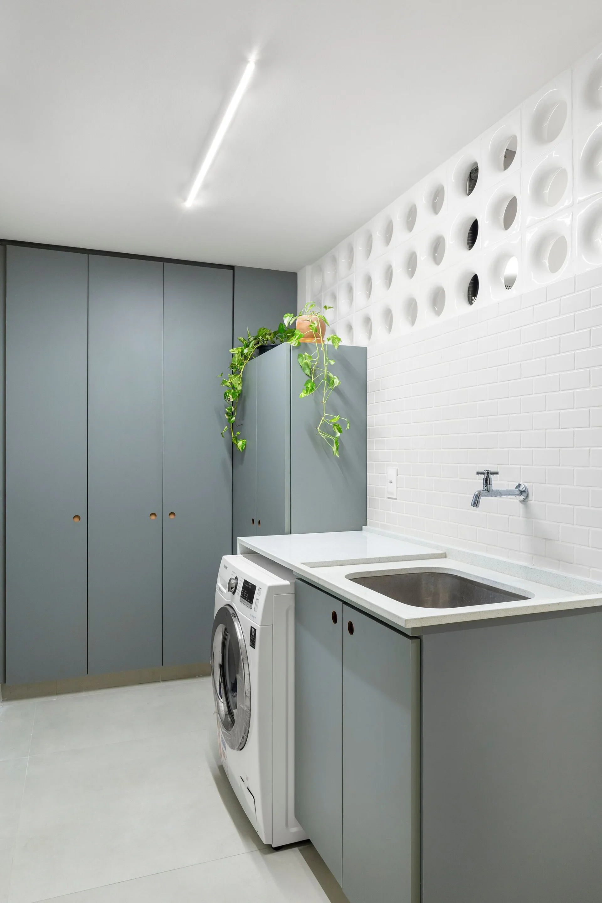 A modern laundry room with matte grey cabinets, a white front-loading washing machine, and a decorative white breezeblock screen wall.