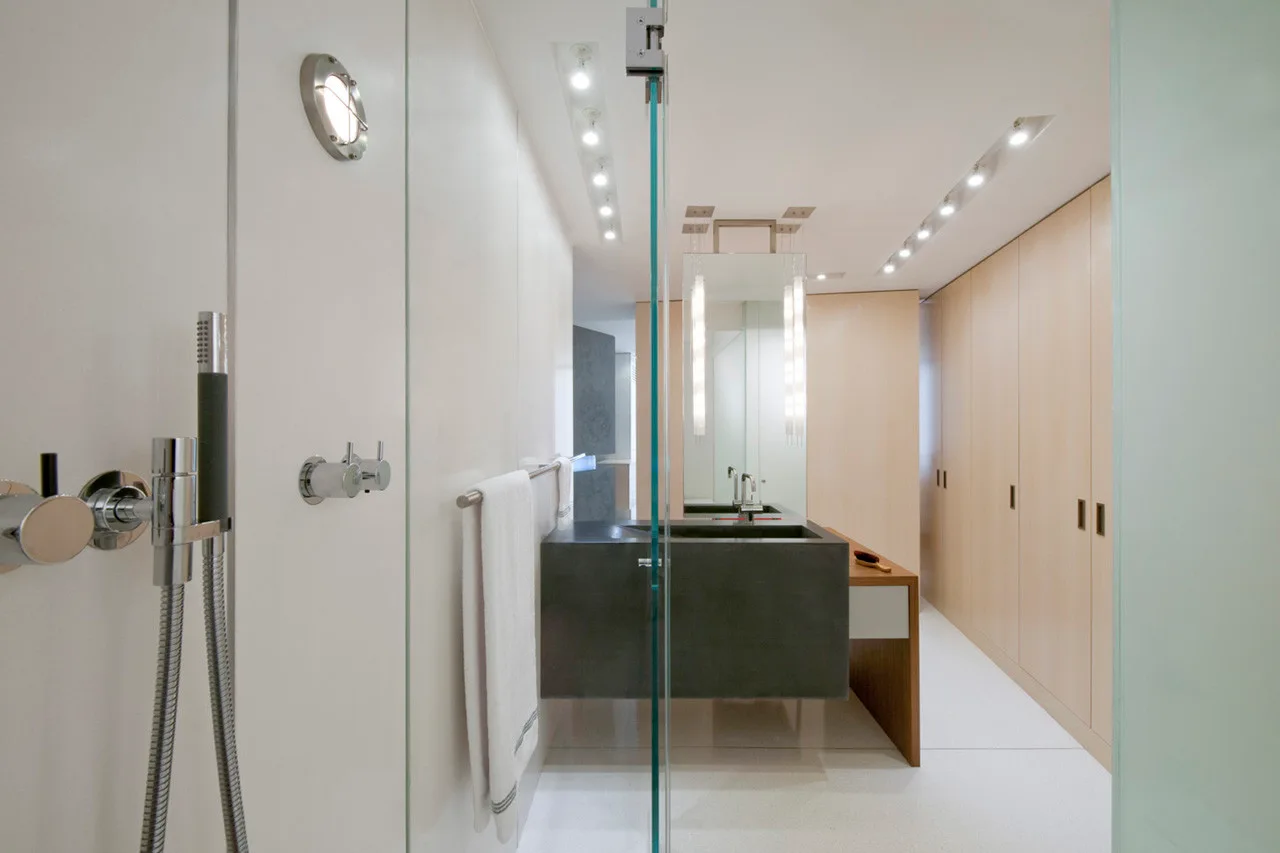 A modern bathroom featuring a dark stone vanity, floor-to-ceiling light wood cabinetry, and a glass shower partition.