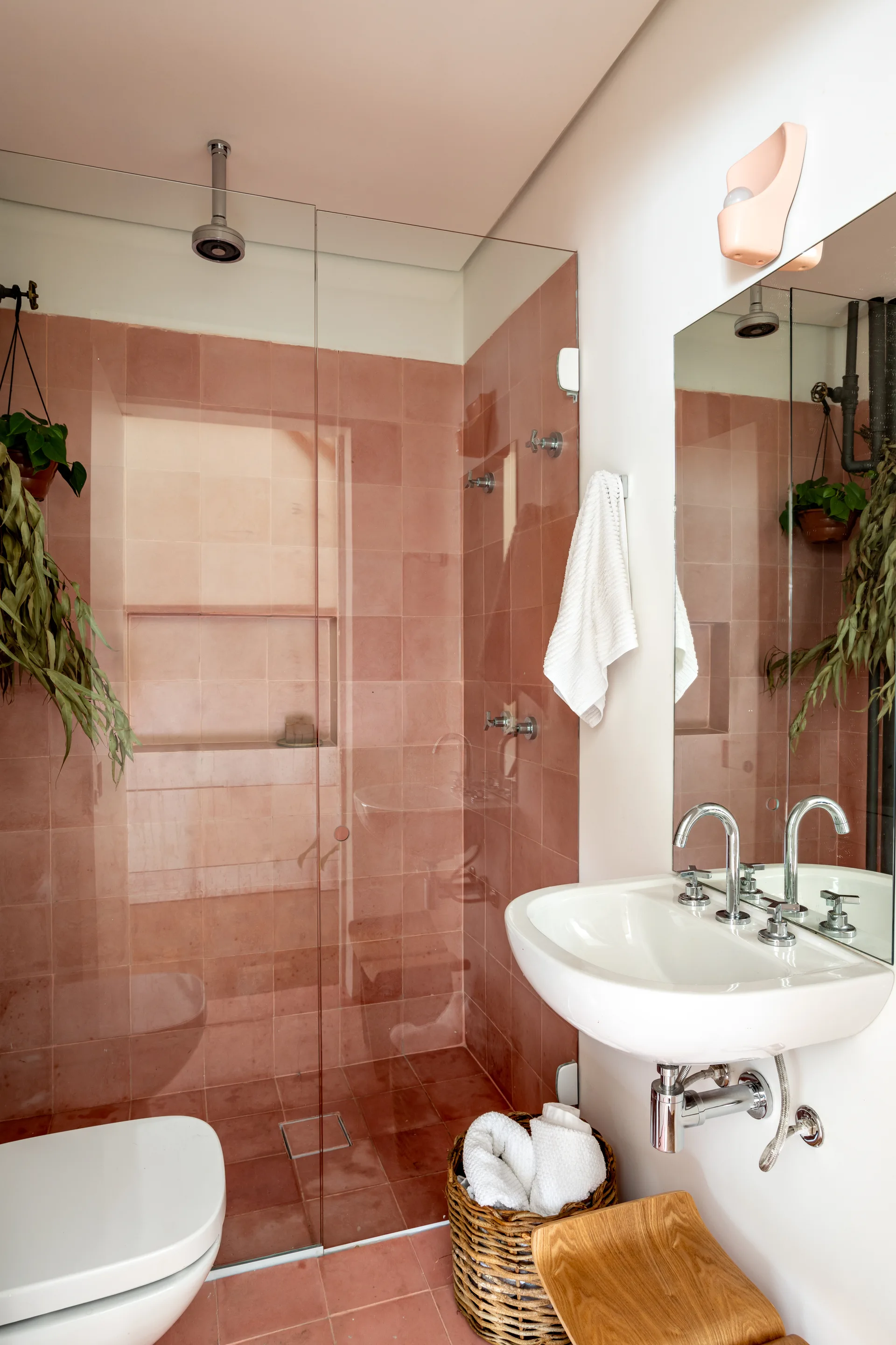 A modern bathroom features a walk-in glass shower lined with pink square tiles next to a white wall-mounted sink.