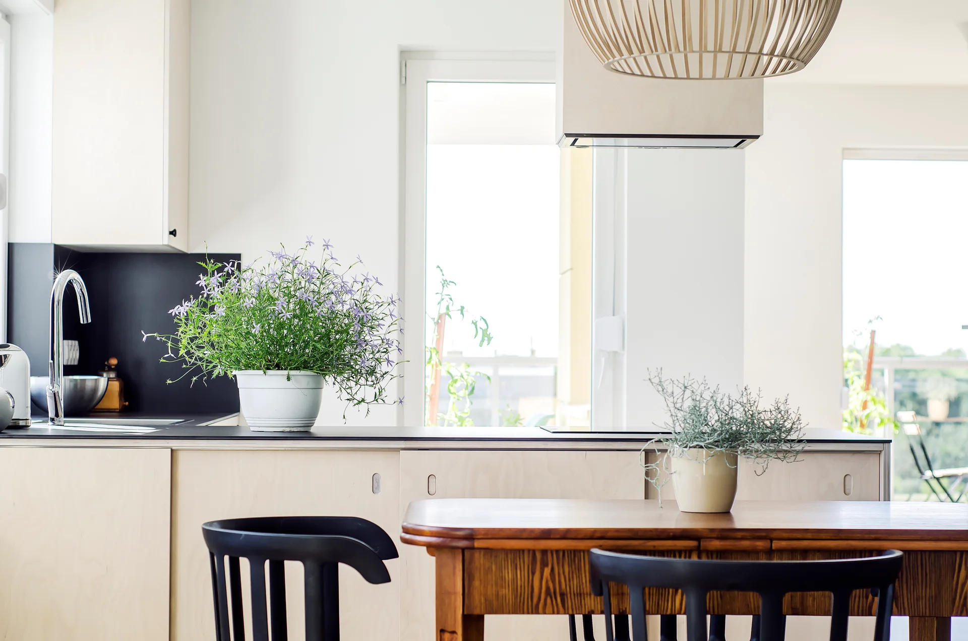 A modern kitchen with flat-front plywood cabinetry, a dark countertop with a silver faucet, and a wooden dining table with black chairs in the foreground.
