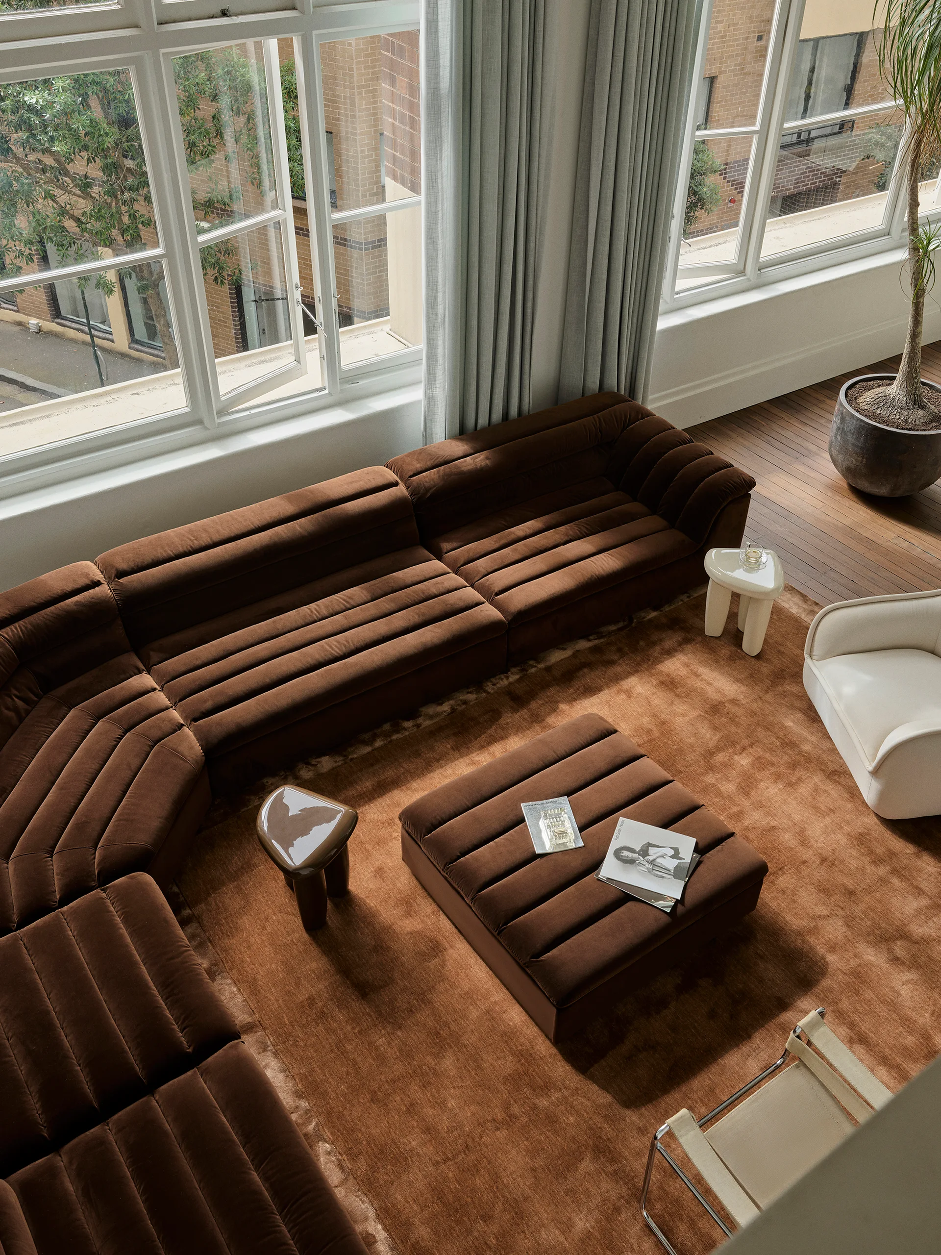 High angle view of a living room featuring a large brown modular sofa with channel tufting, a matching ottoman, and a plush brown rug.