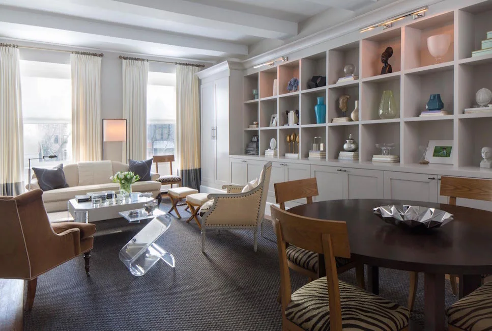 An open-plan living and dining room featuring a large off-white built-in grid shelving unit, a dark wood dining table, and zebra print chairs.