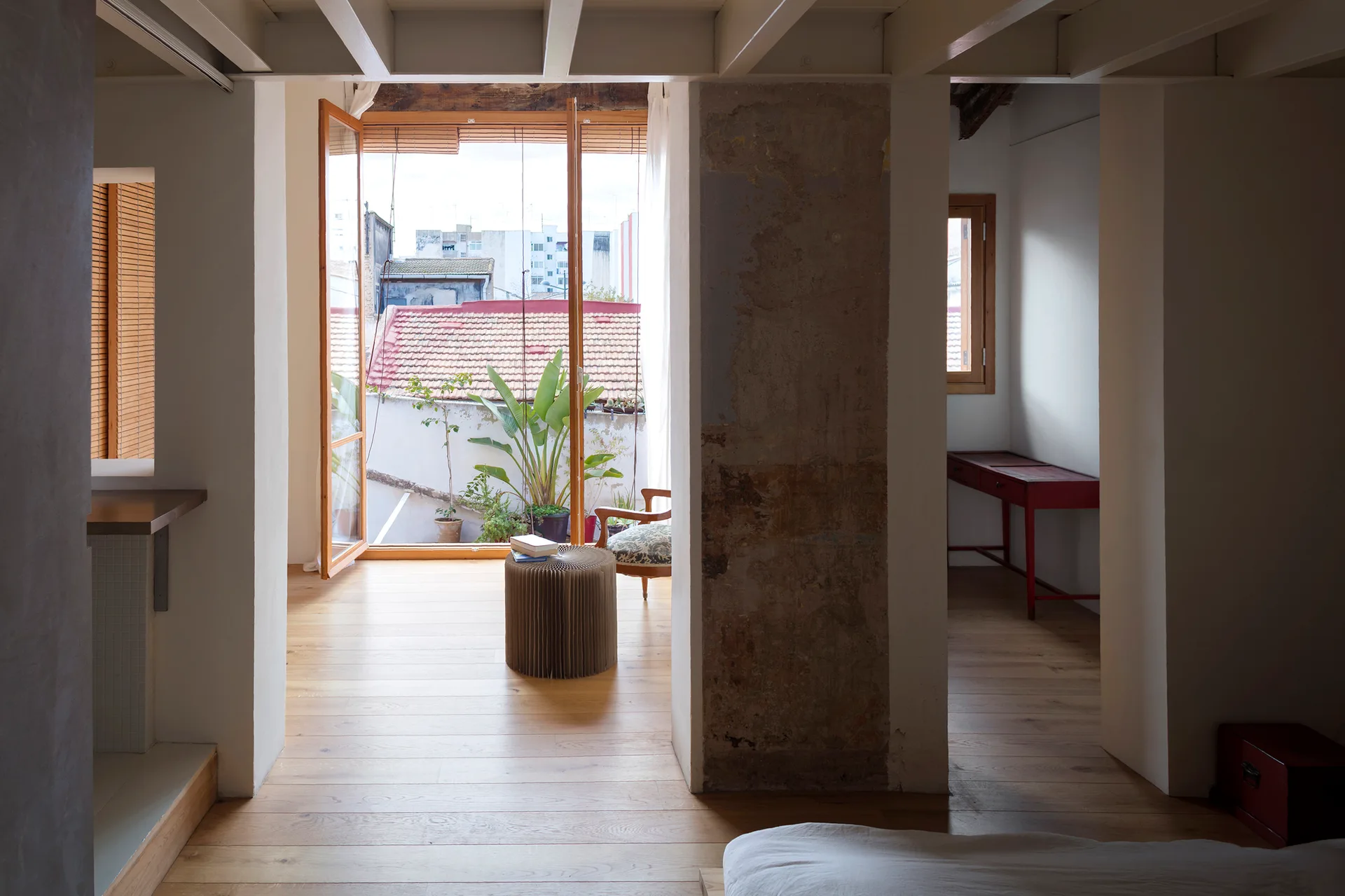 An airy apartment interior with light wood floors, an exposed concrete column, and open balcony doors.