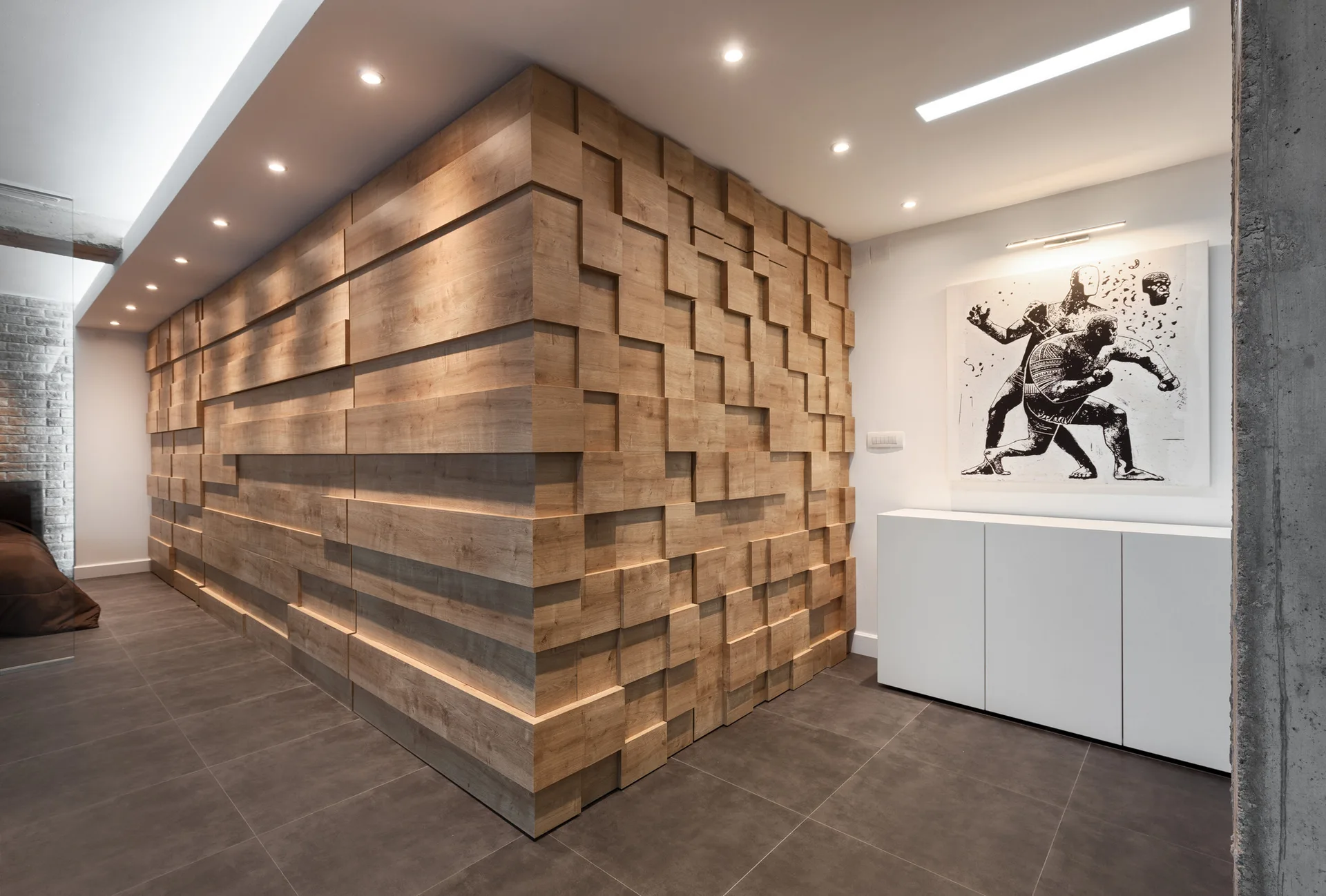 A modern corridor features a corner wall covered in three-dimensional wood blocks next to a white storage cabinet with graphic wall art.